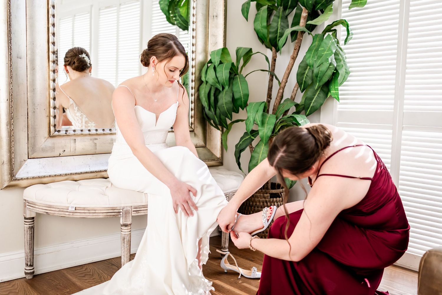 Wedding dress preparation scene with indoor plants and vintage mirror in background.