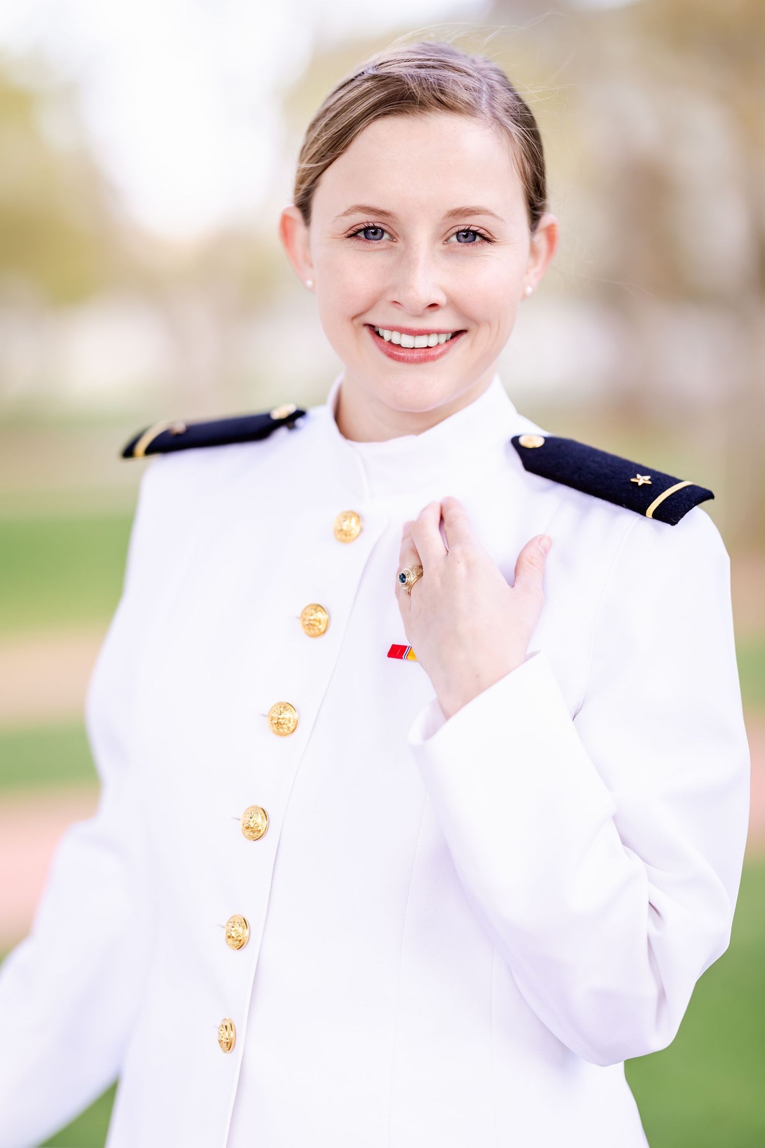 Naval officer in crisp white dress uniform with gold buttons stands outdoors in natural lighting.