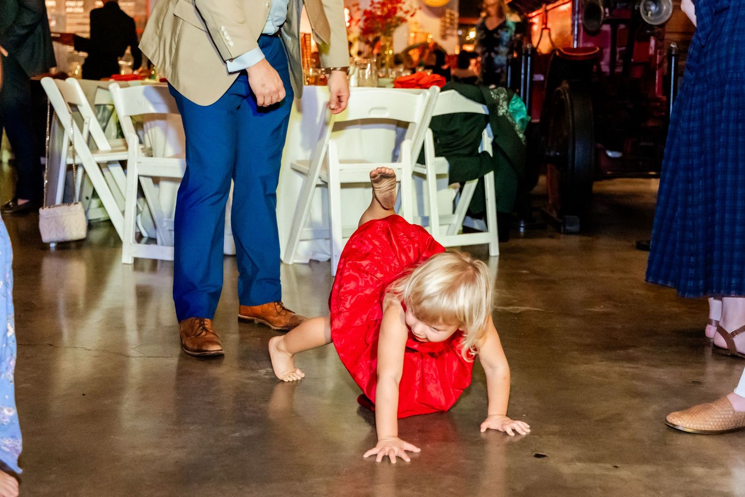 Young child in red dress crawling on dance floor during wedding reception.