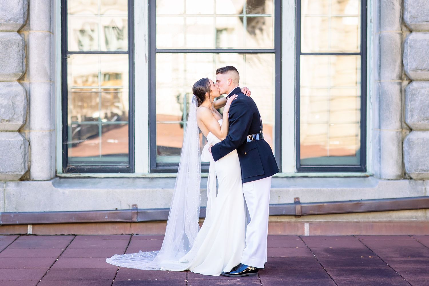 A romantic wedding couple shares a tender moment in front of large stone windows on their special day.