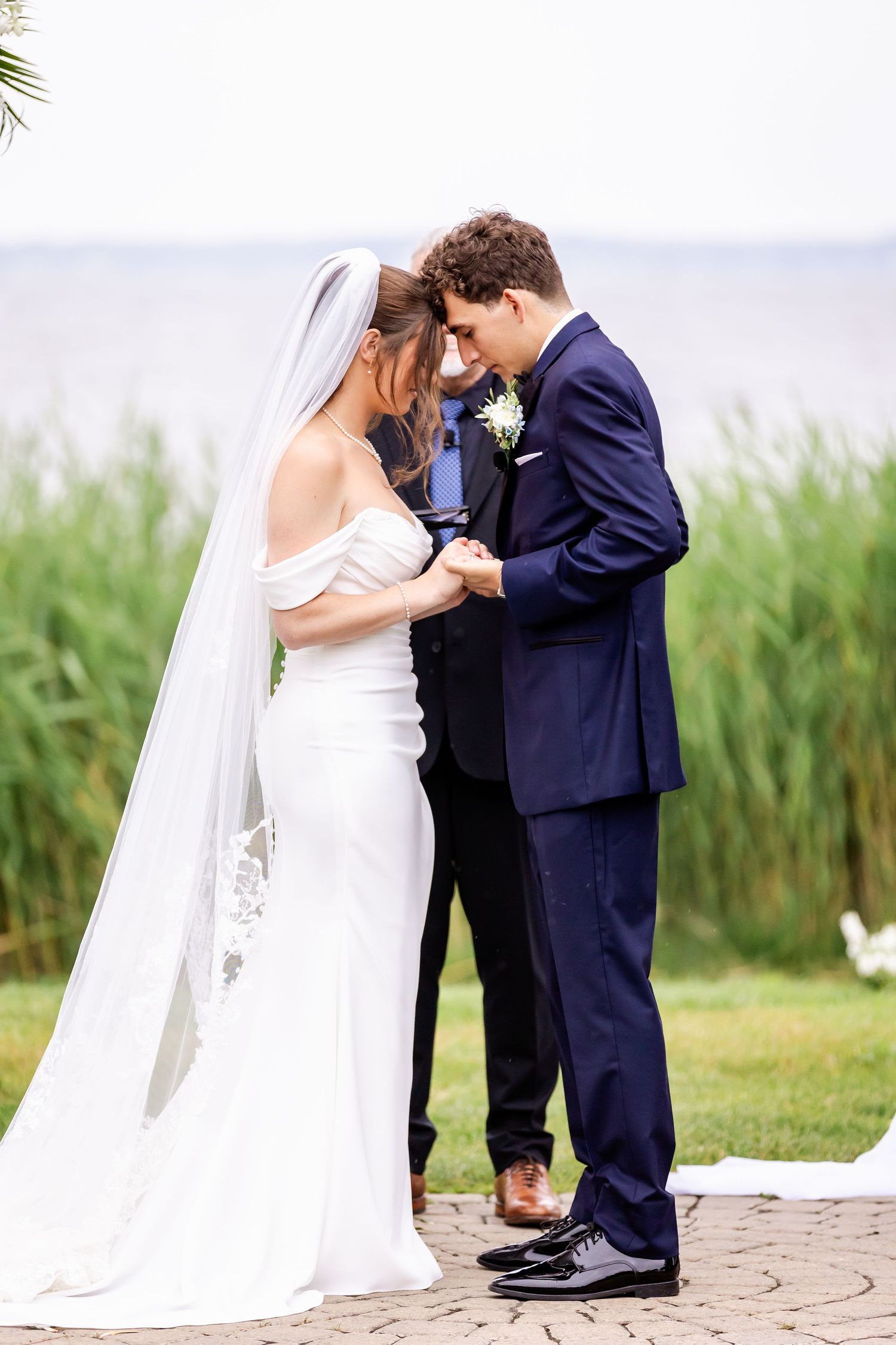 A romantic wedding couple shares an intimate moment together by a lakeside with tall reeds in the background.