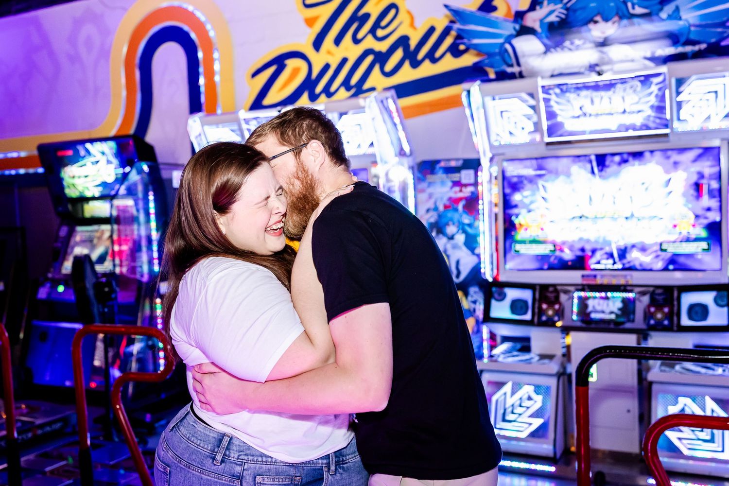 Couple embraces in front of neon arcade machines and colorful lights at The Drive-In entertainment venue.