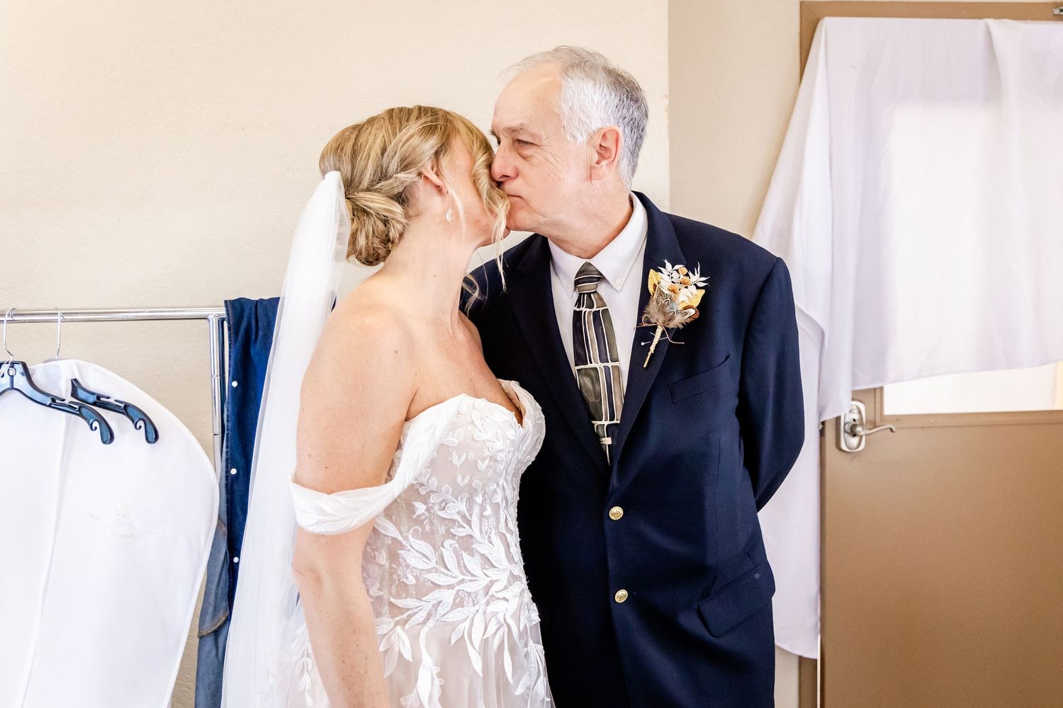 Intimate wedding moment between bride in white lace dress and guest in navy suit with boutonniere.