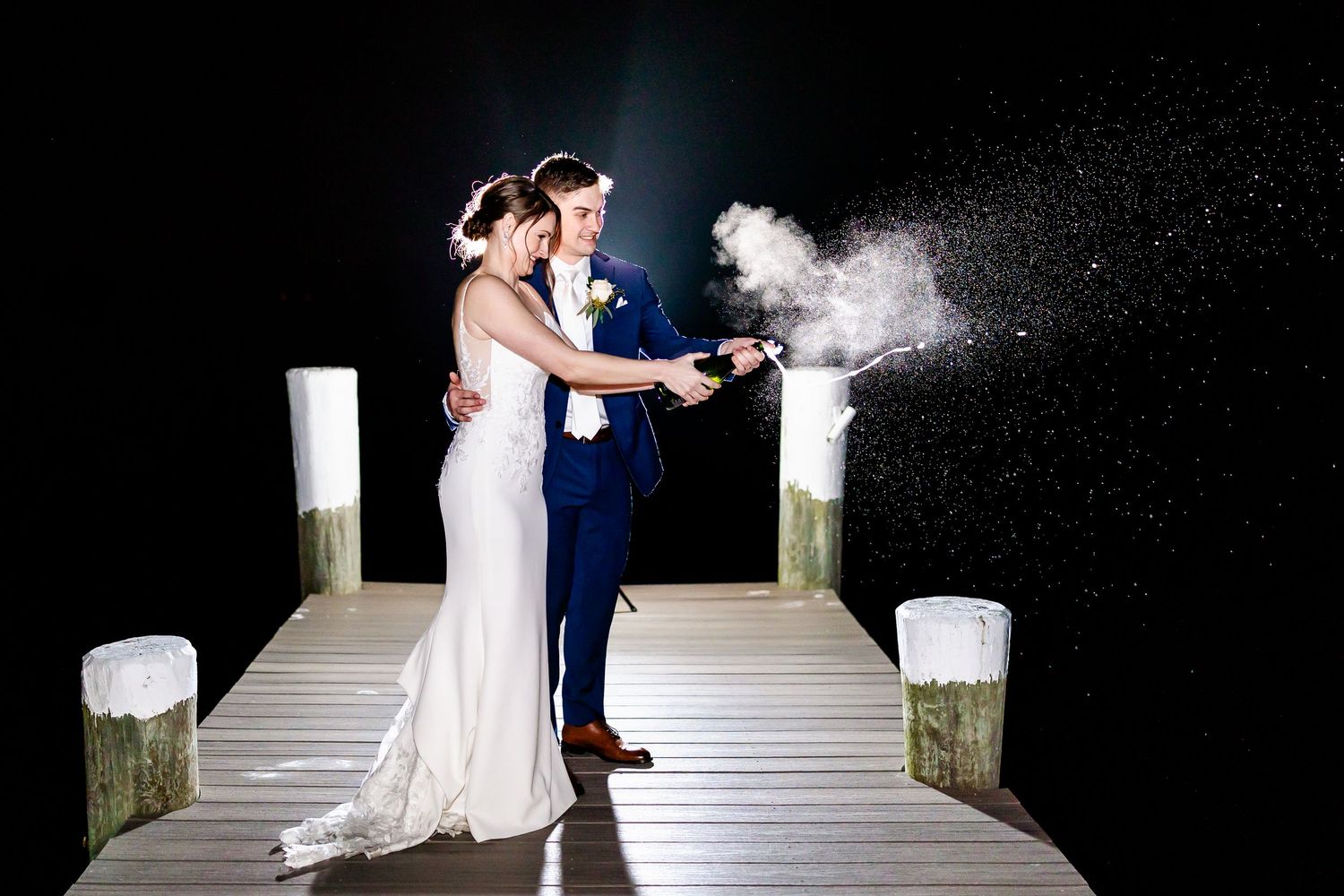Romantic nighttime wedding photos on a dock with dramatic lighting and mist effects.