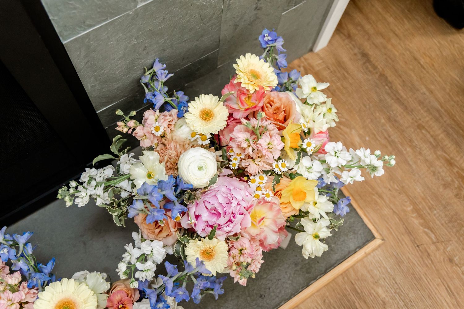 Wedding bouquet with pastel flowers and blue delphiniums on wooden floor.