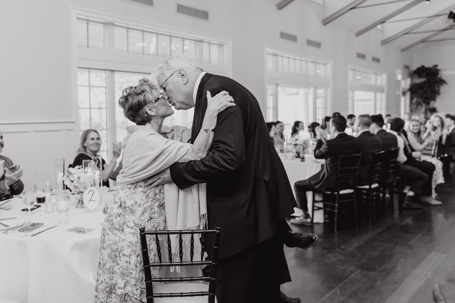 A couple dances together at an elegant wedding reception in a bright indoor venue.