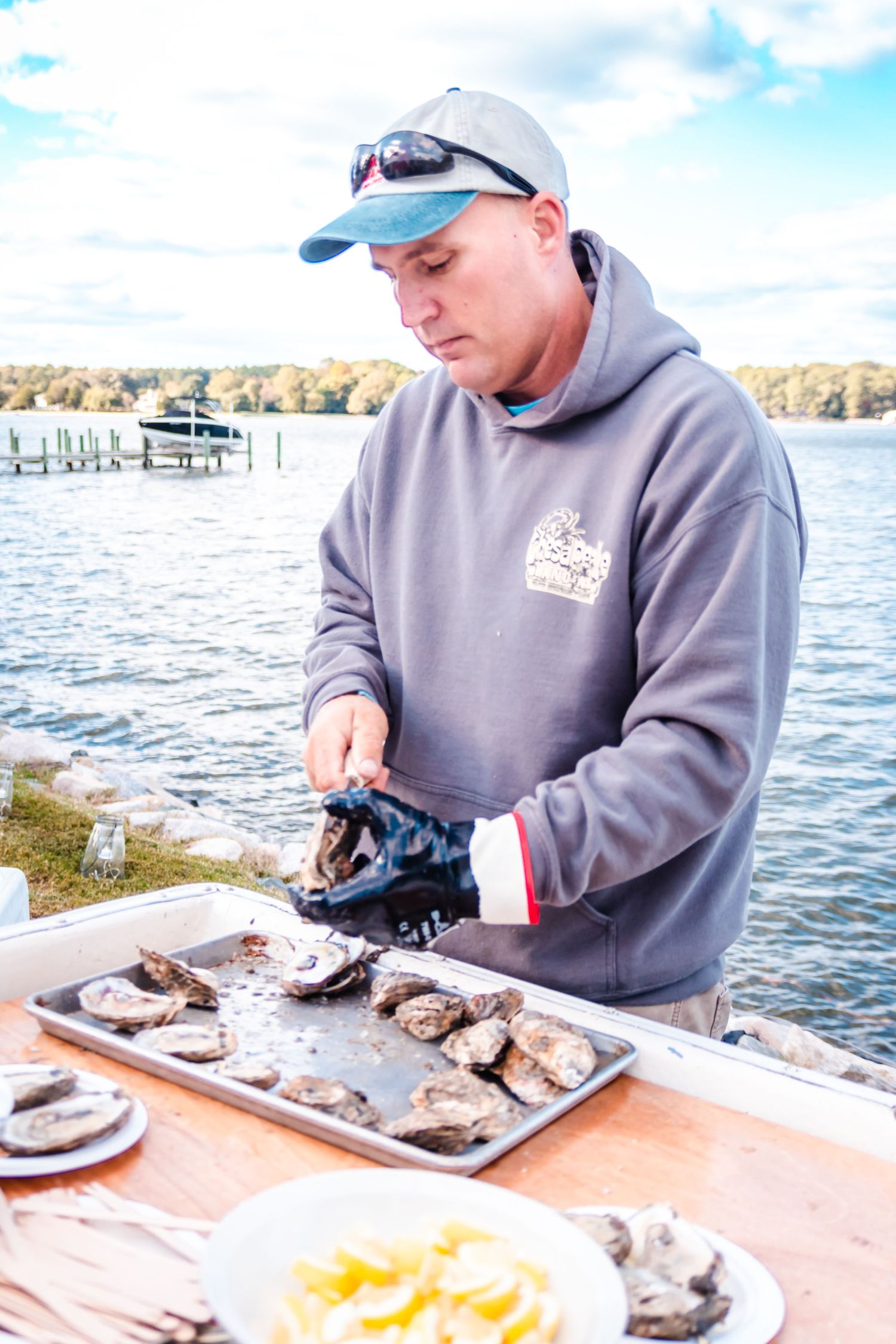 Person shucking fresh oysters at waterfront dock with lemons and serving tray on sunny autumn day.
