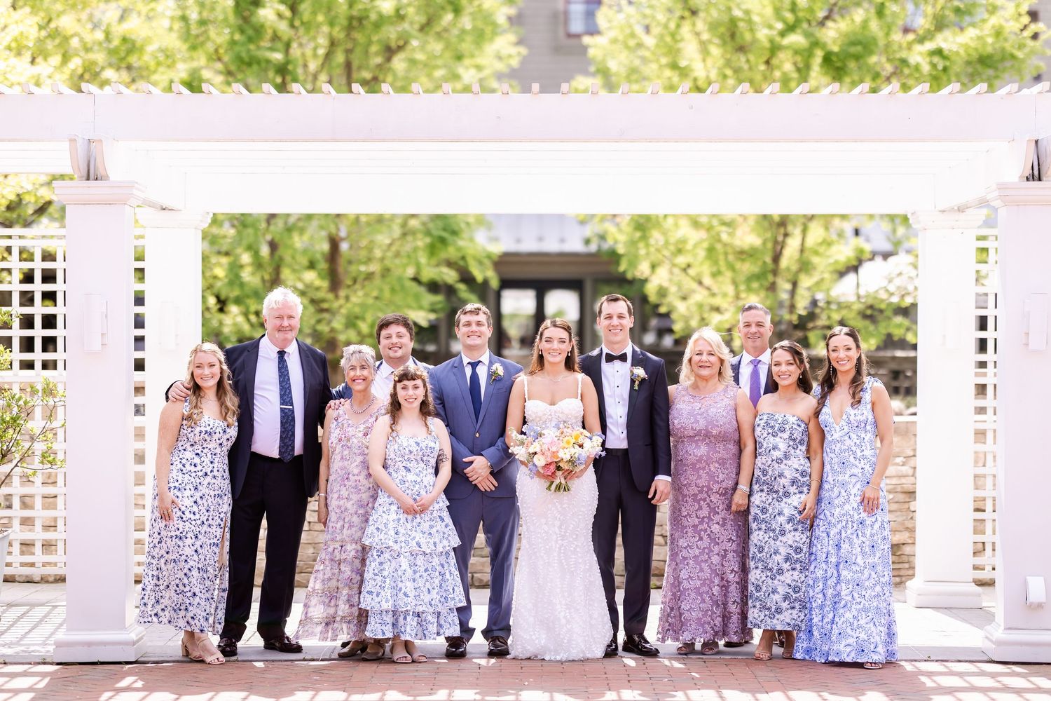 Wedding party poses under white pergola wearing coordinated blue and purple floral attire.
