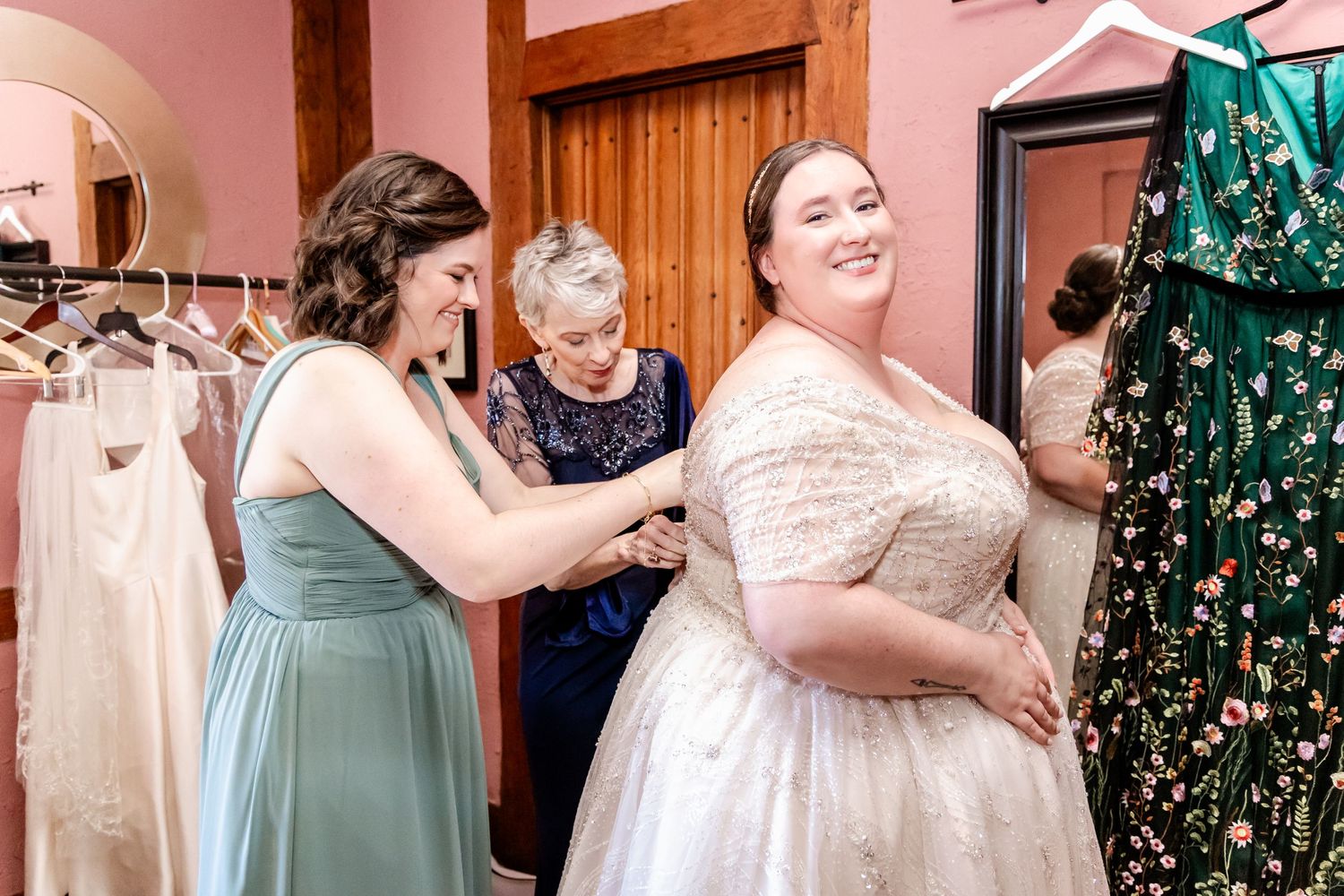 Wedding dress fitting scene with bridesmaids helping adjust the gown in a bridal boutique.
