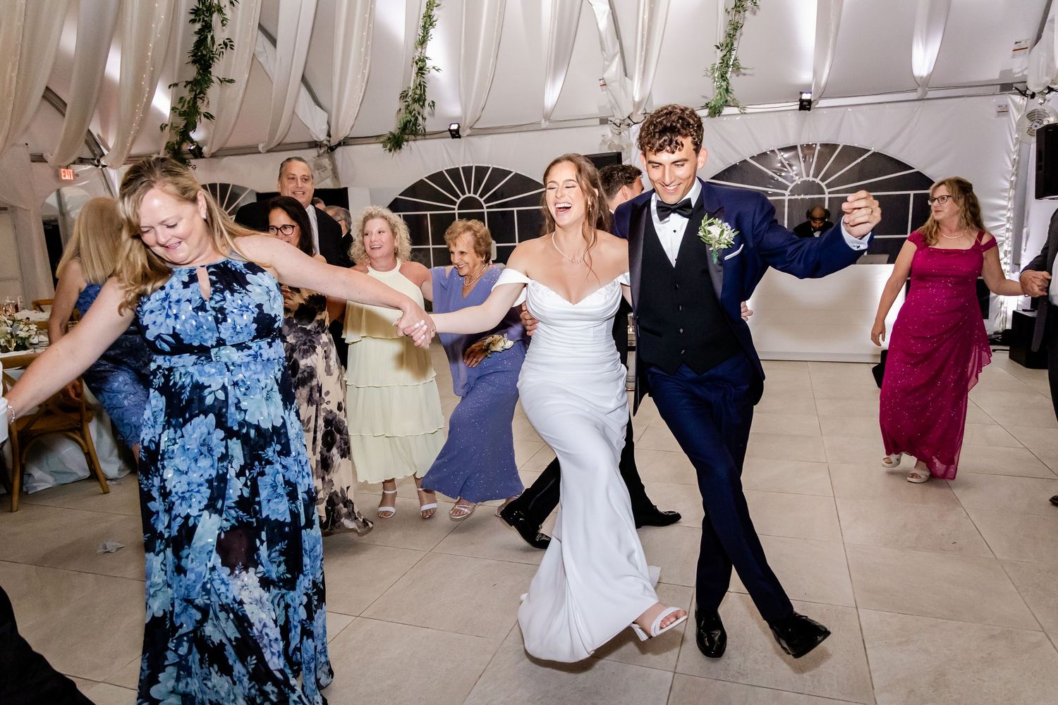 Wedding guests dancing and celebrating on a decorated dance floor under a white tent.