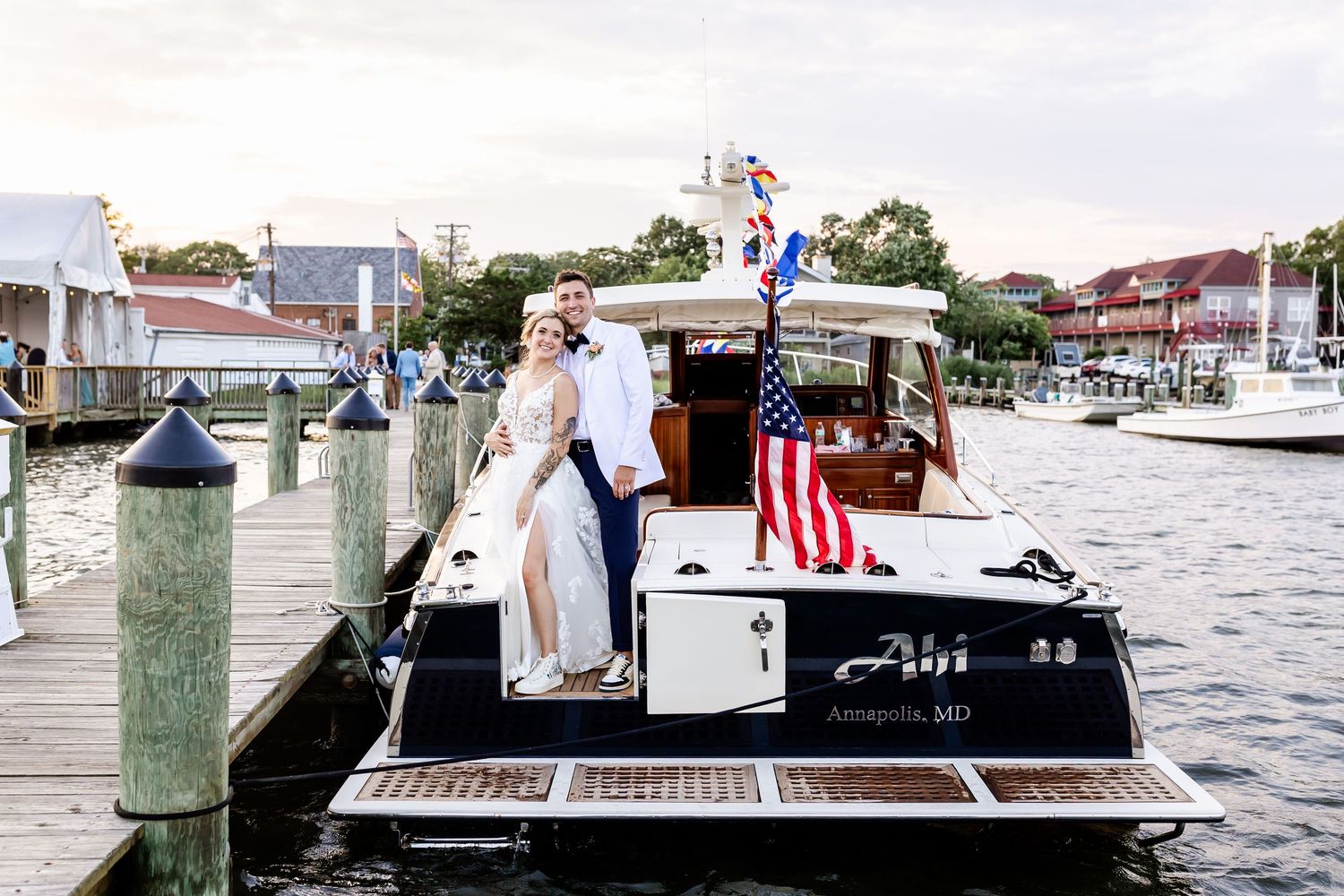 A couple stands together on a boat dock near a white vessel in a marina on a cloudy day.