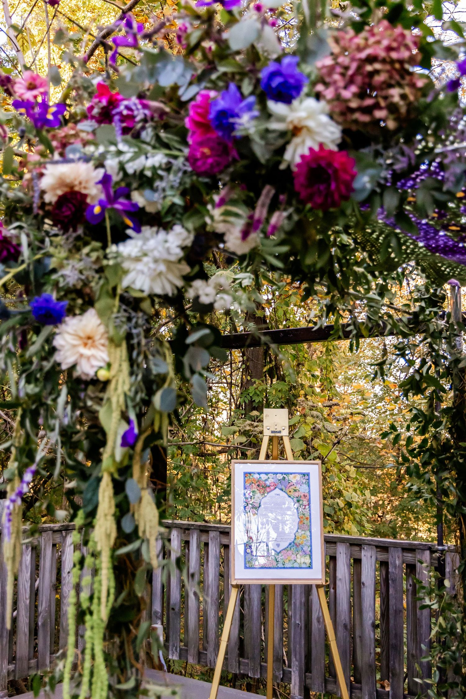 Vibrant purple and white floral arrangement frames an art display on an easel in a garden setting.
