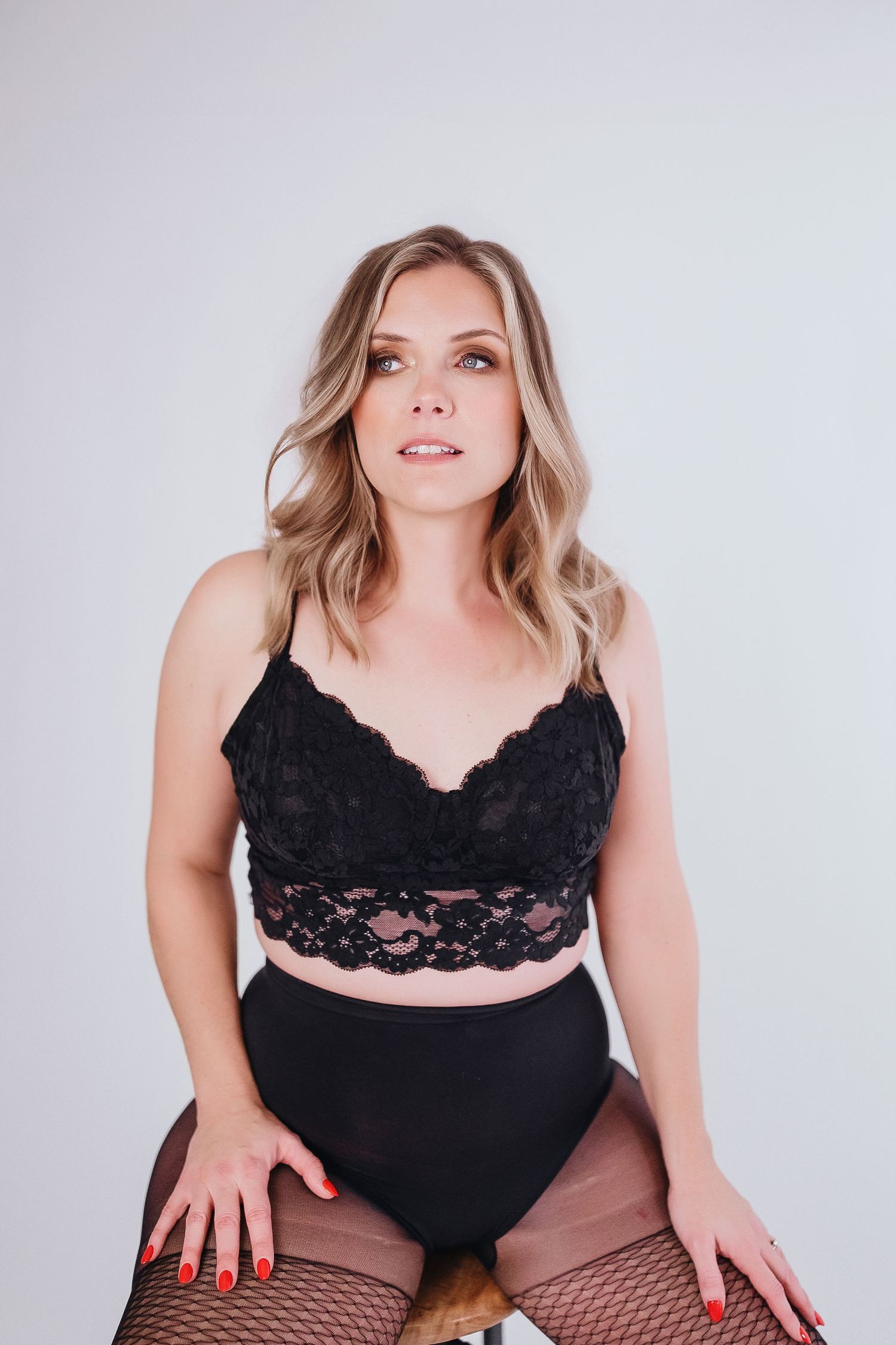 Boudoir portrait featuring black lace top and fishnet stockings against white backdrop.