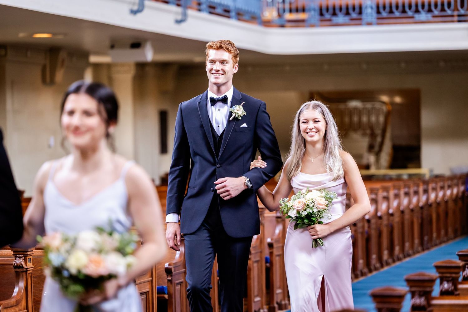 Wedding ceremony procession in church sanctuary with traditional wooden pews.