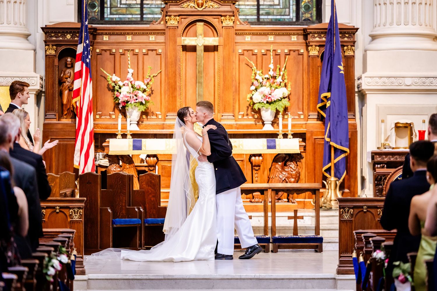 Newlyweds share their first kiss at the altar in a church decorated with flags and flowers.
