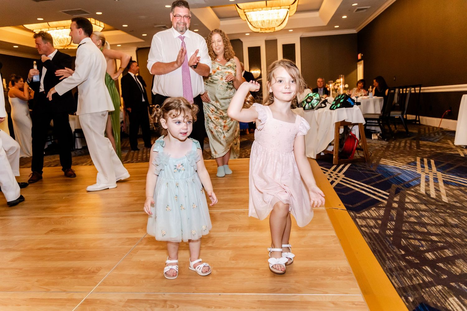 Children and guests dancing on wooden floor during wedding reception celebration.