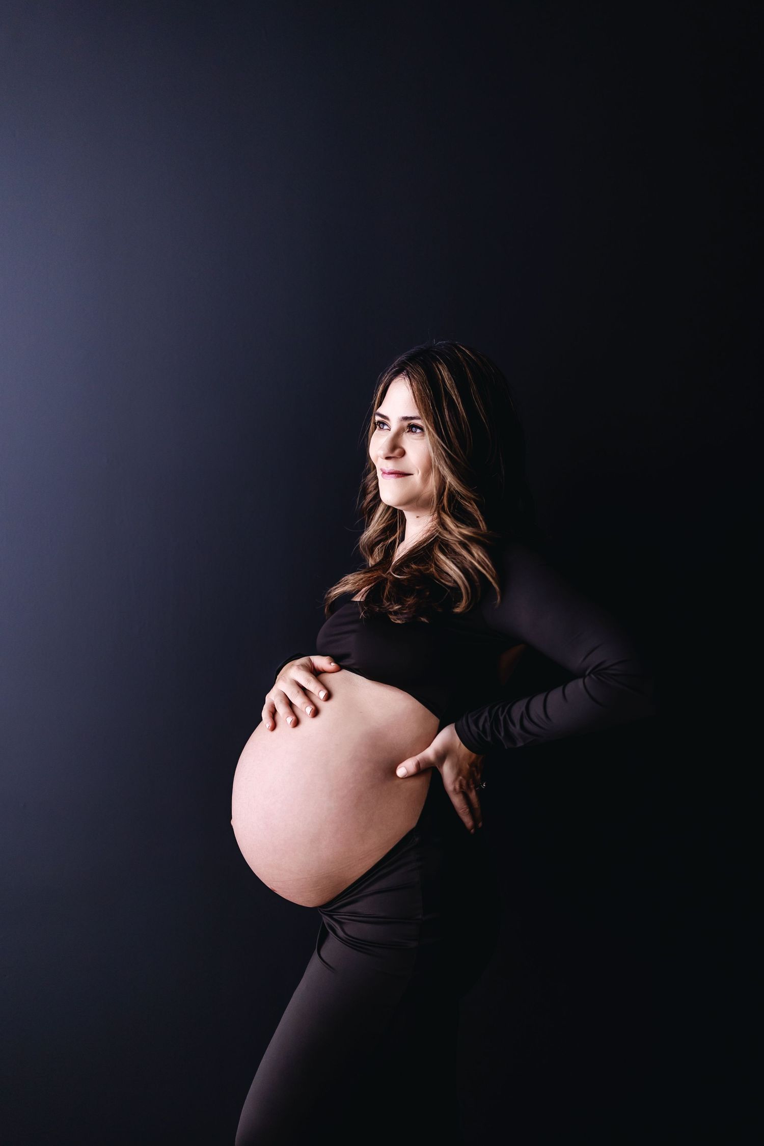 Creative maternity photography with dramatic lighting highlighting the baby bump.
