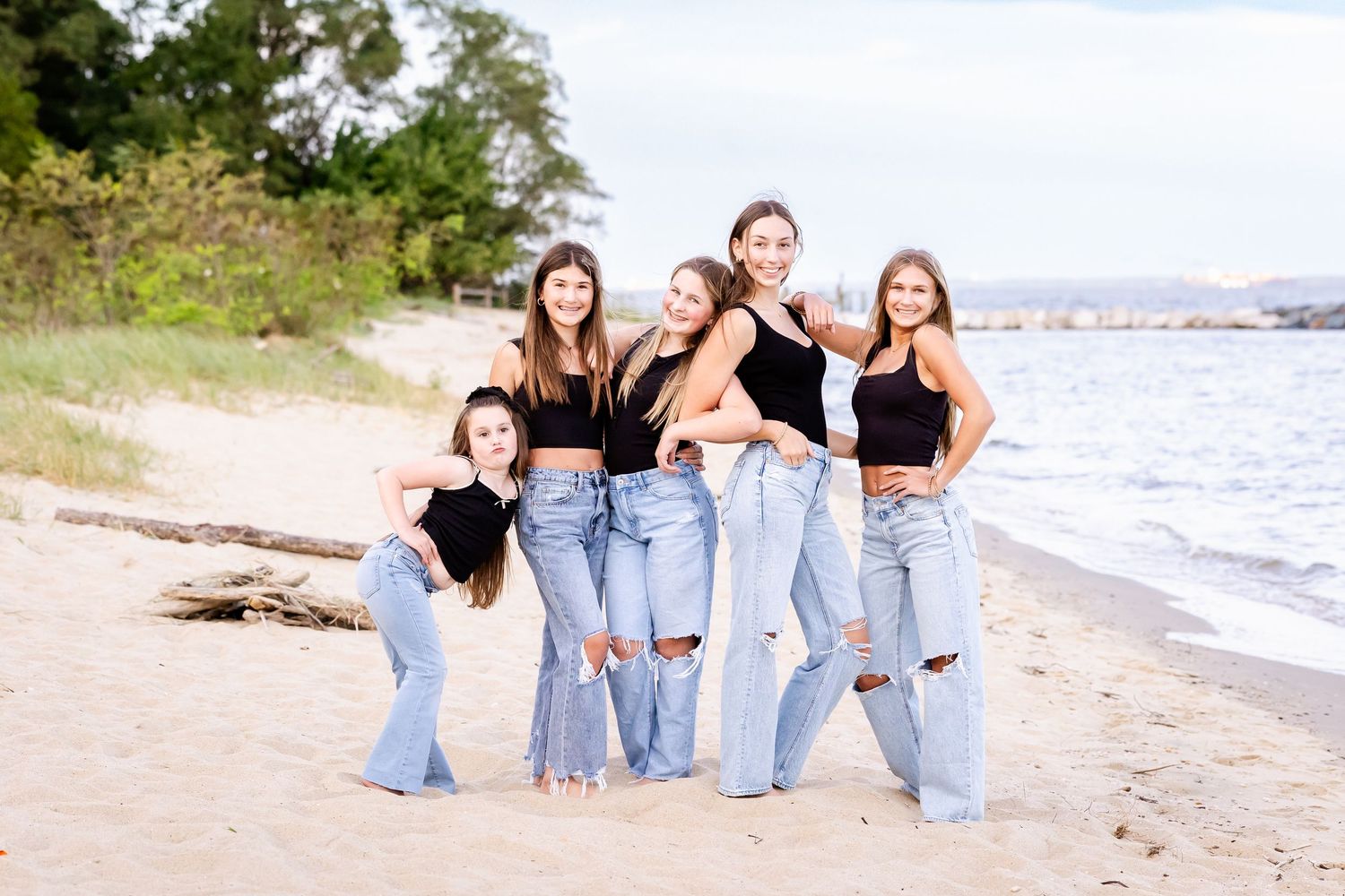 A group in matching denim and black outfits laughs together while posing on a sunny beach.