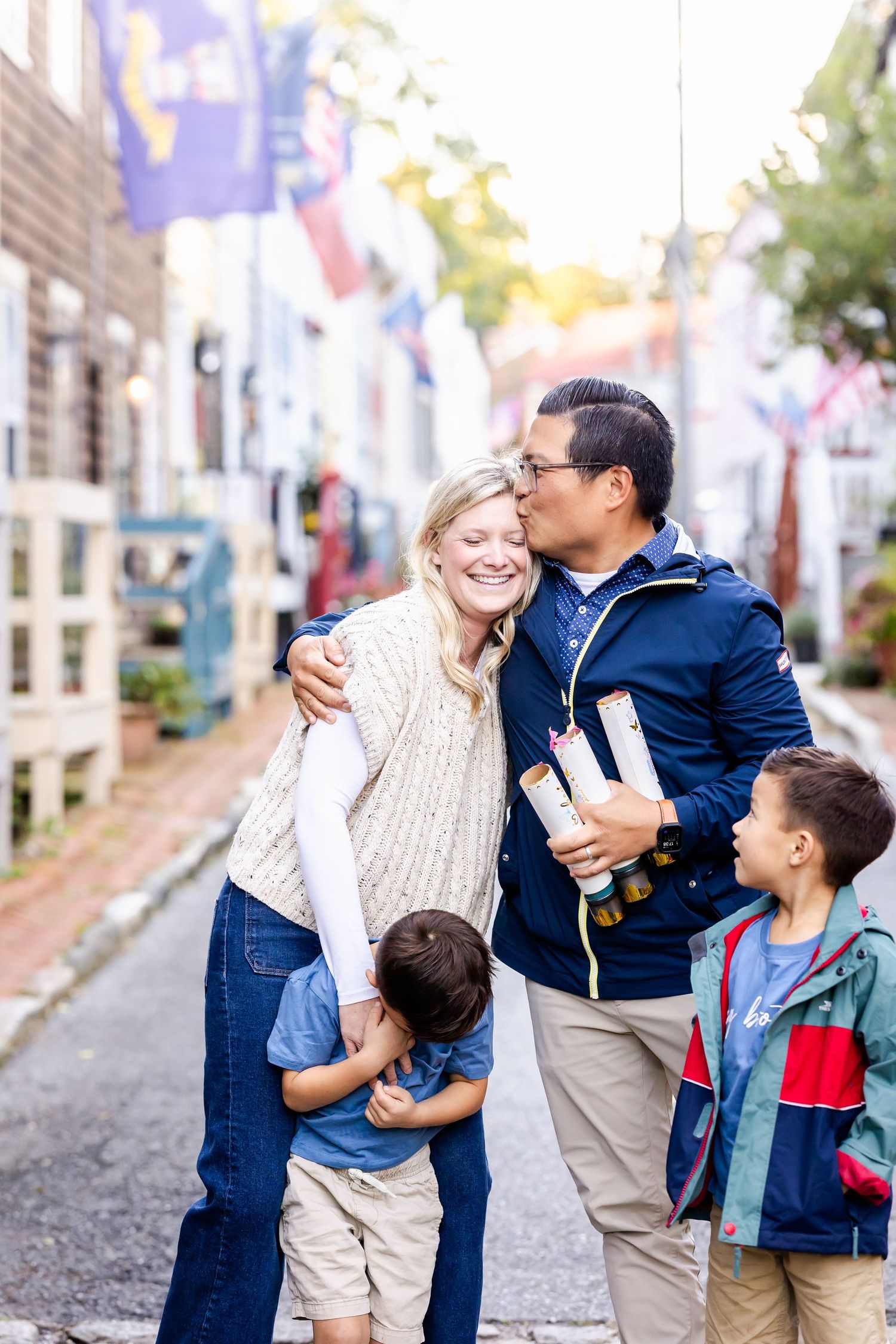 A happy family embraces and laughs together on a charming cobblestone street with colorful buildings in the background.