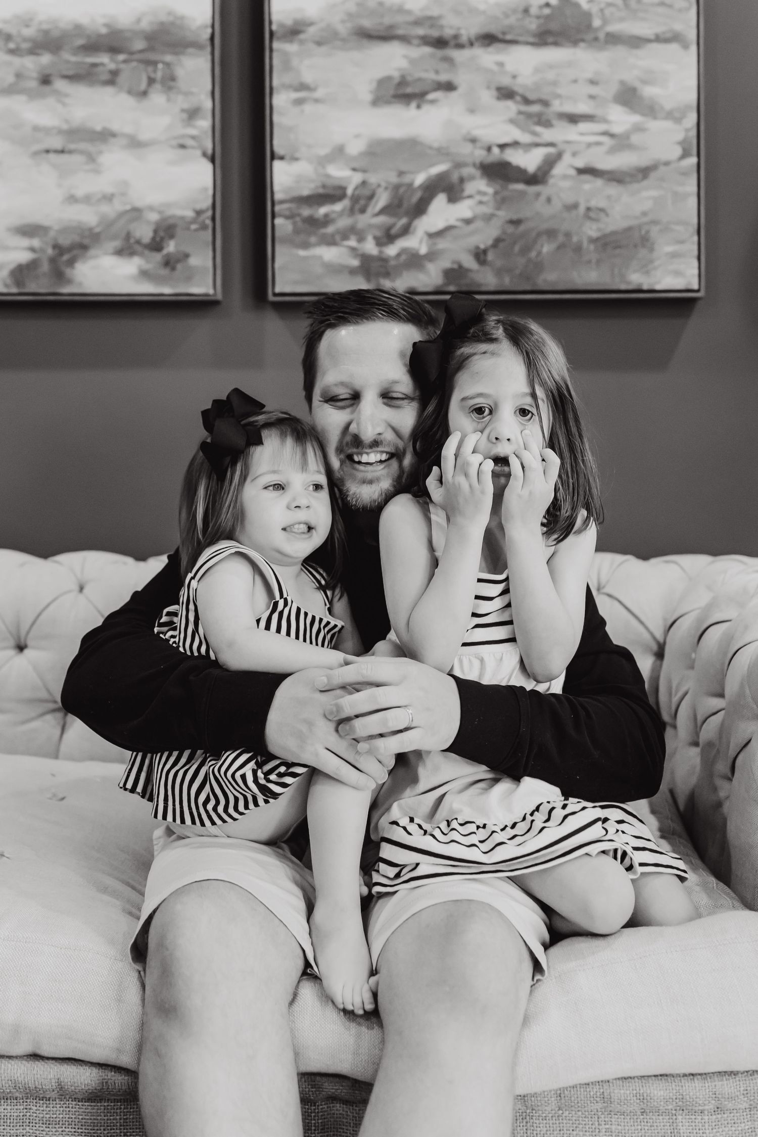 A black and white photo of a loving family moment on a couch with two children in striped dresses.