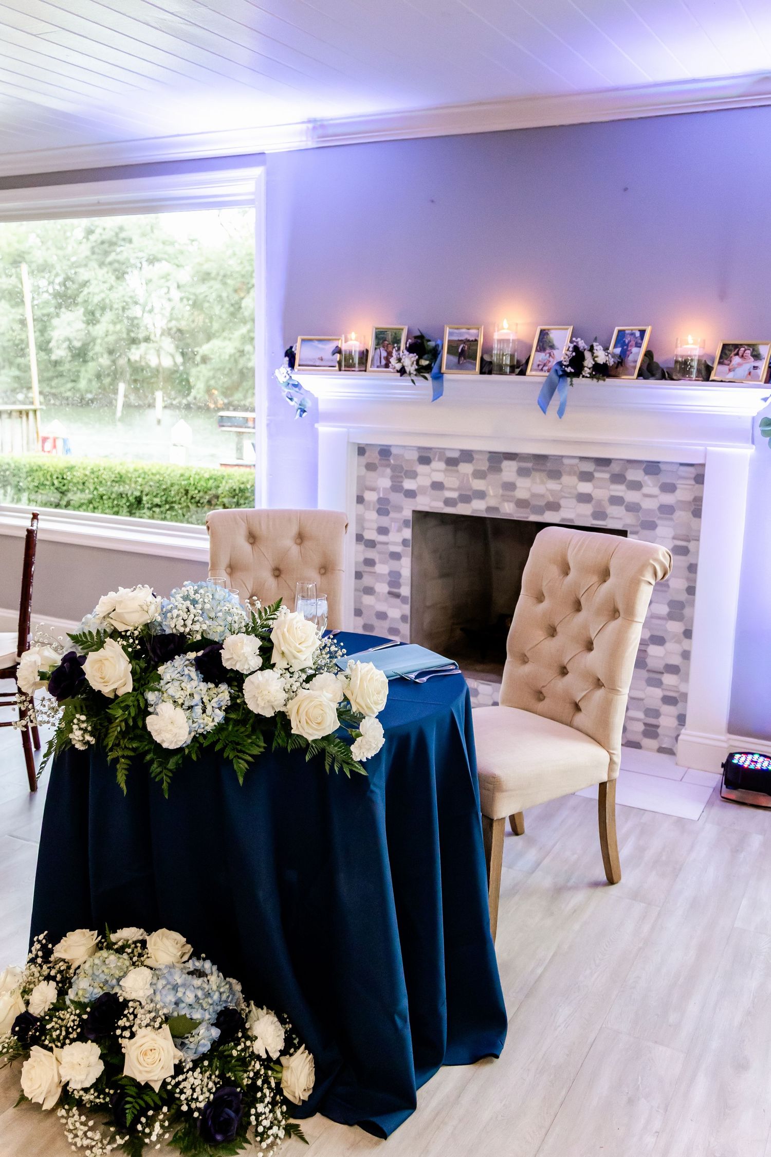 Wedding reception tables with navy blue linens and white floral centerpieces in an elegant white room.