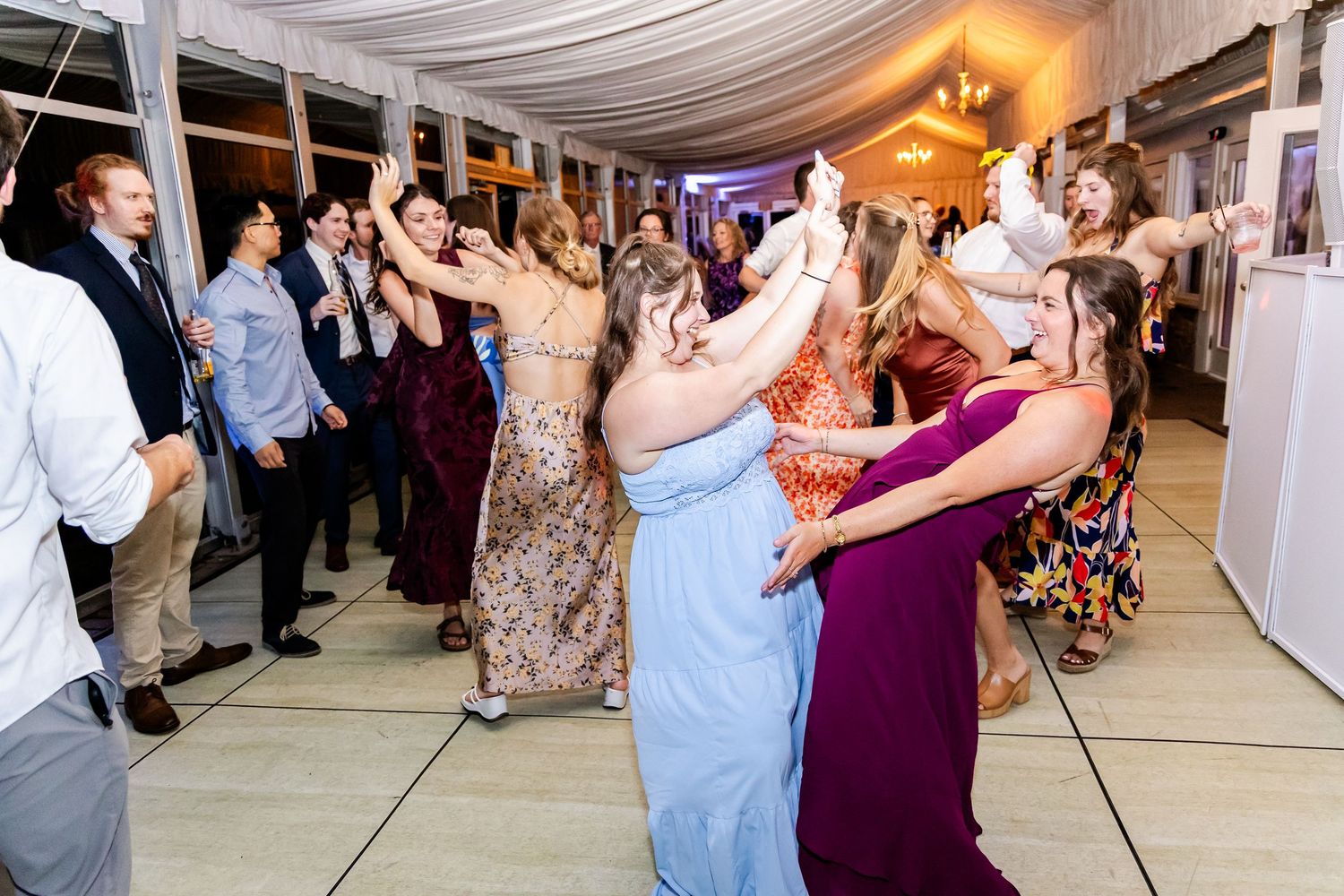 Wedding guests dancing and celebrating in a white tent reception space.