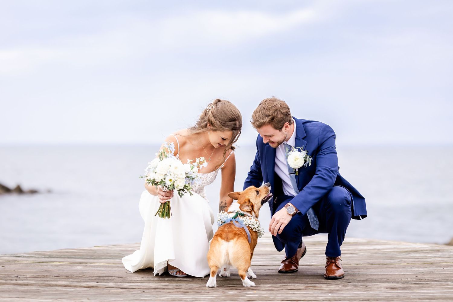 Wedding couple posing with their dog on wooden pier by the water.