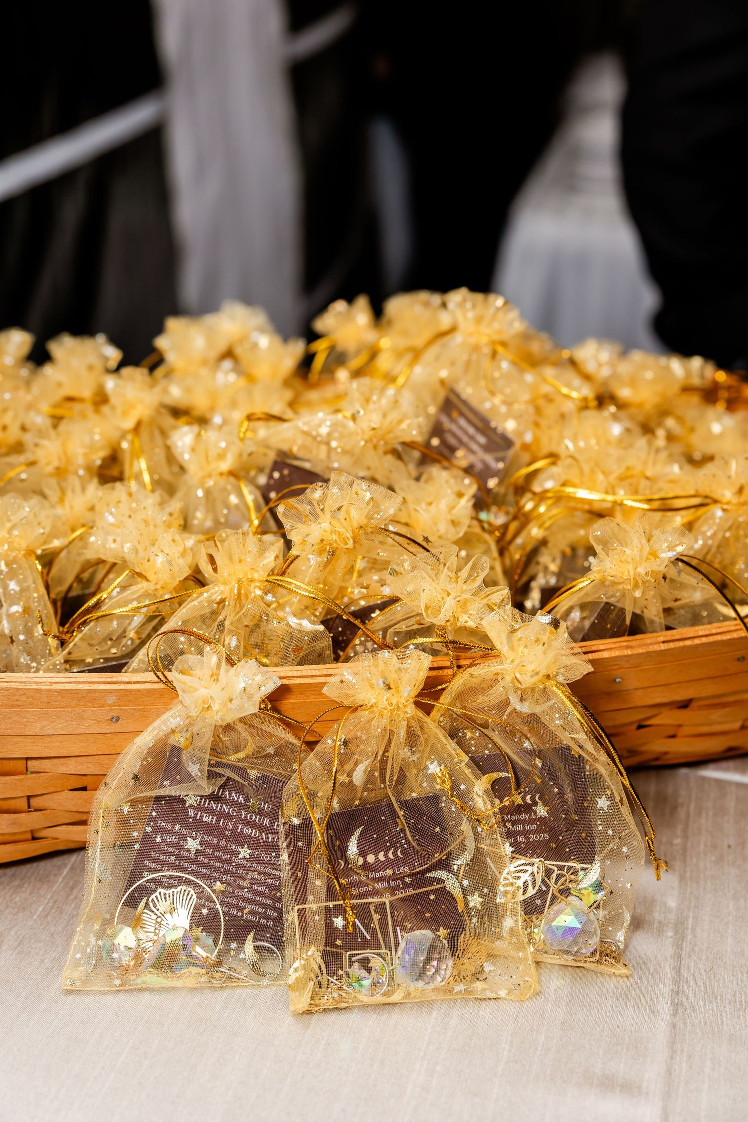 Small gift bags with gold bows arranged in wicker baskets at a wedding favor display.
