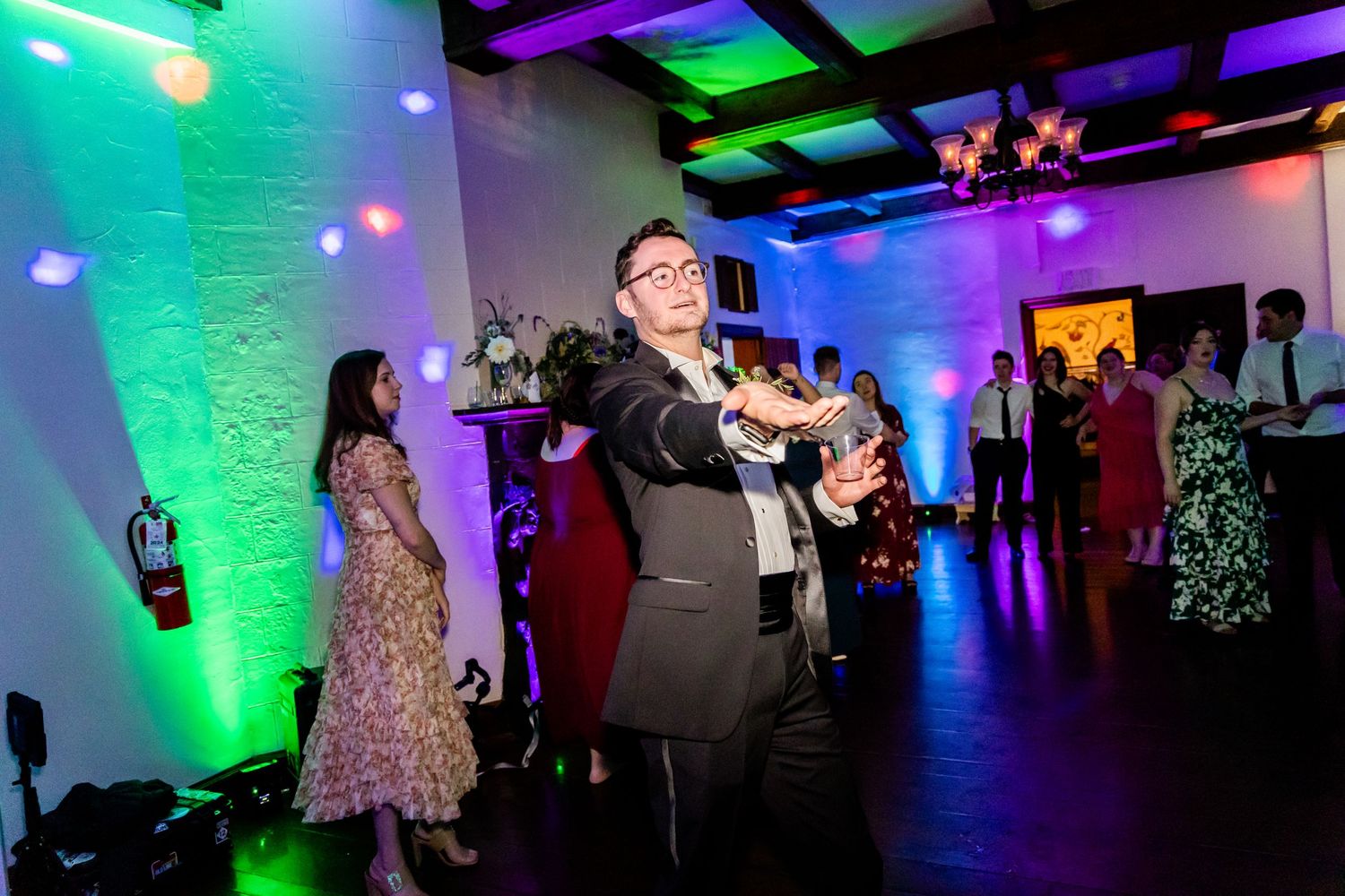 Wedding guests dancing and celebrating under colorful neon lights in a reception venue.