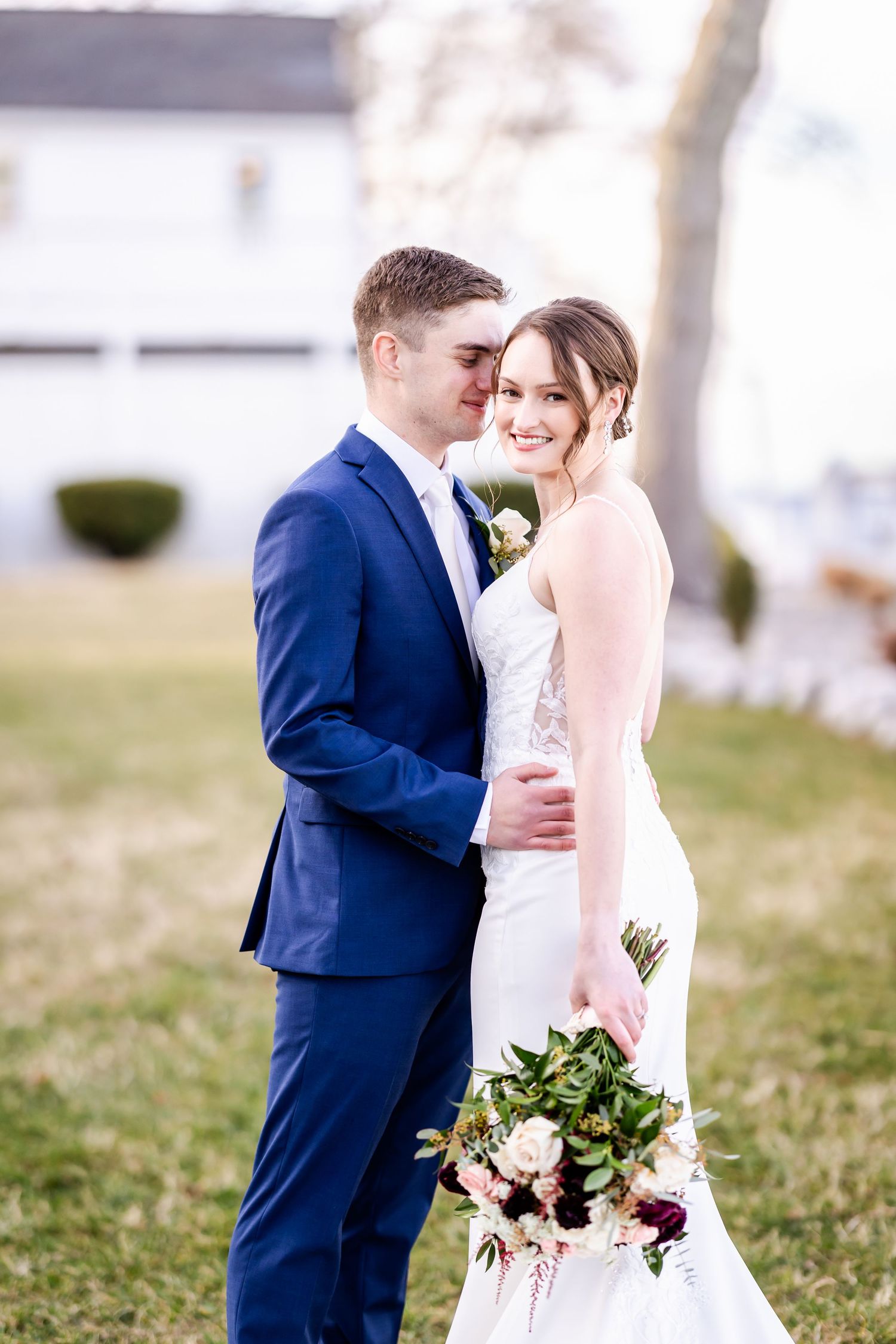 Romantic wedding couple poses outdoors with bride in white dress and groom in navy suit.