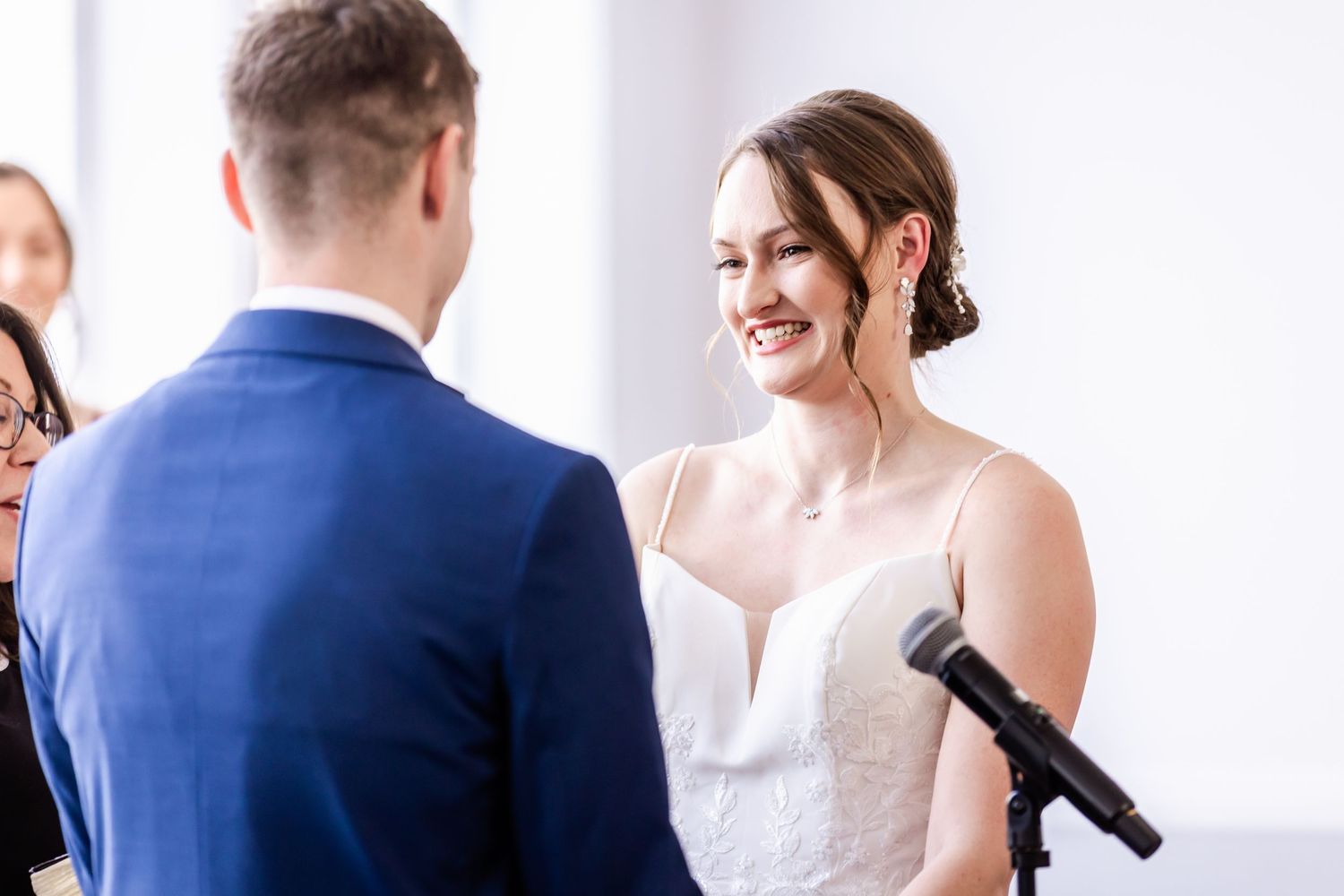 Wedding ceremony participants standing in a bright white room during speeches or toasts.