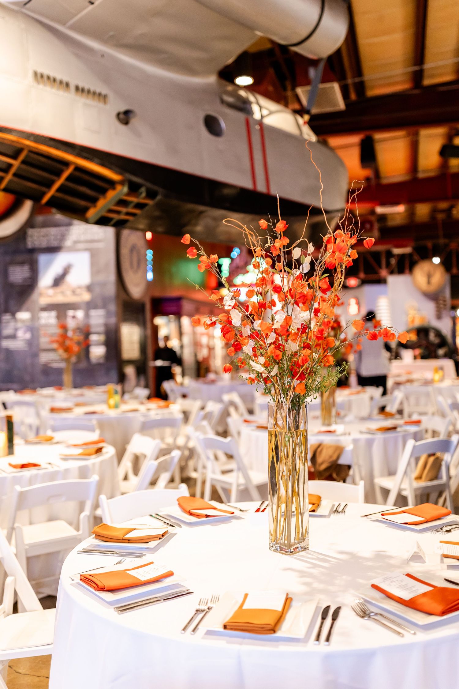 Round tables decorated with orange floral centerpieces and white linens set for an elegant reception dinner.