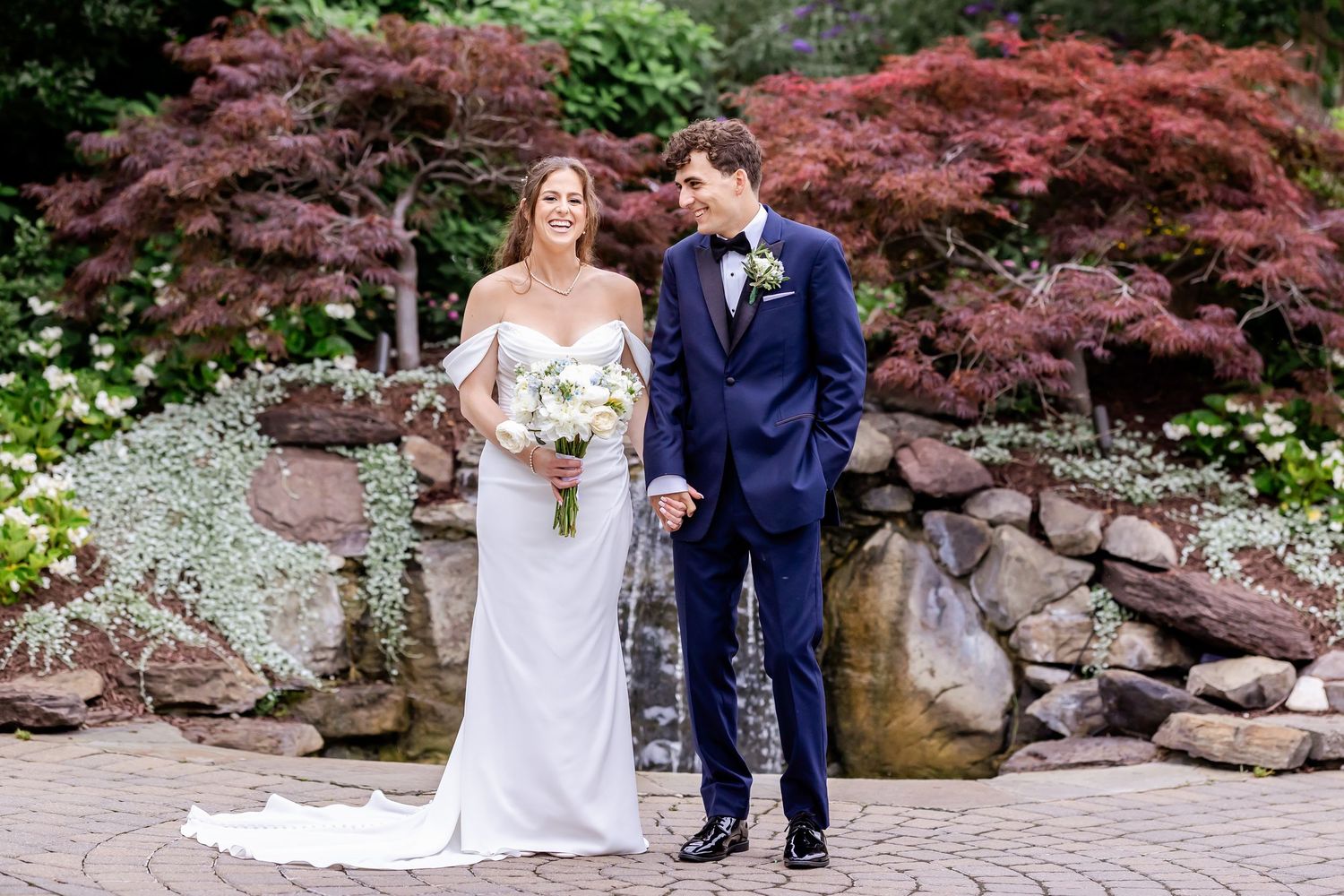 A couple poses together in a garden with vibrant red Japanese maple trees creating a romantic backdrop.