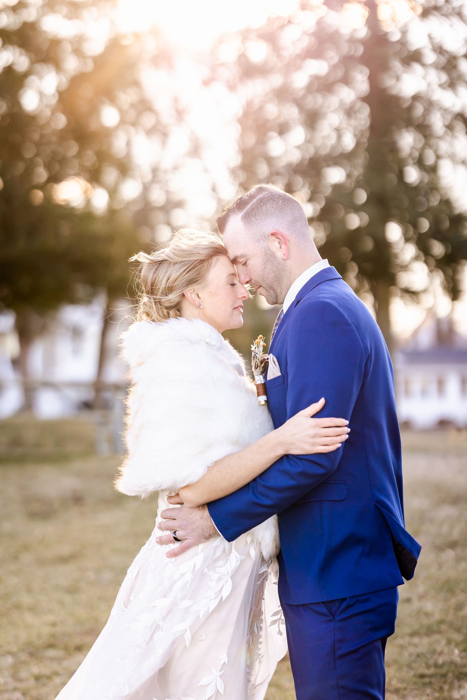 A romantic winter wedding scene with a couple in white dress and blue suit embracing outdoors at sunset.