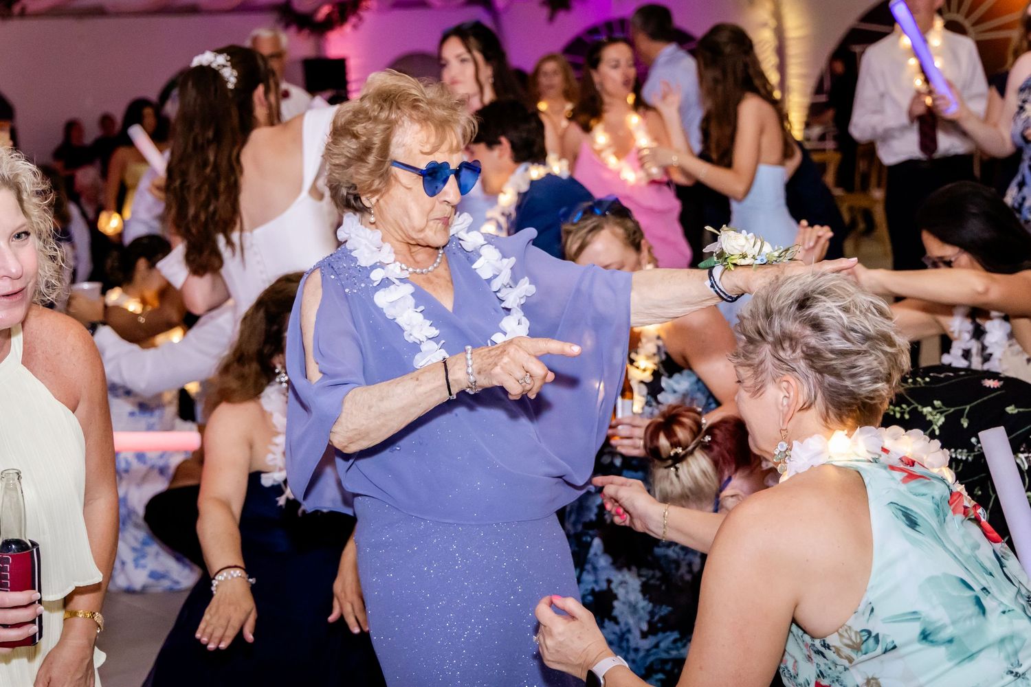 Wedding reception dance floor filled with guests enjoying the celebration under purple lighting.