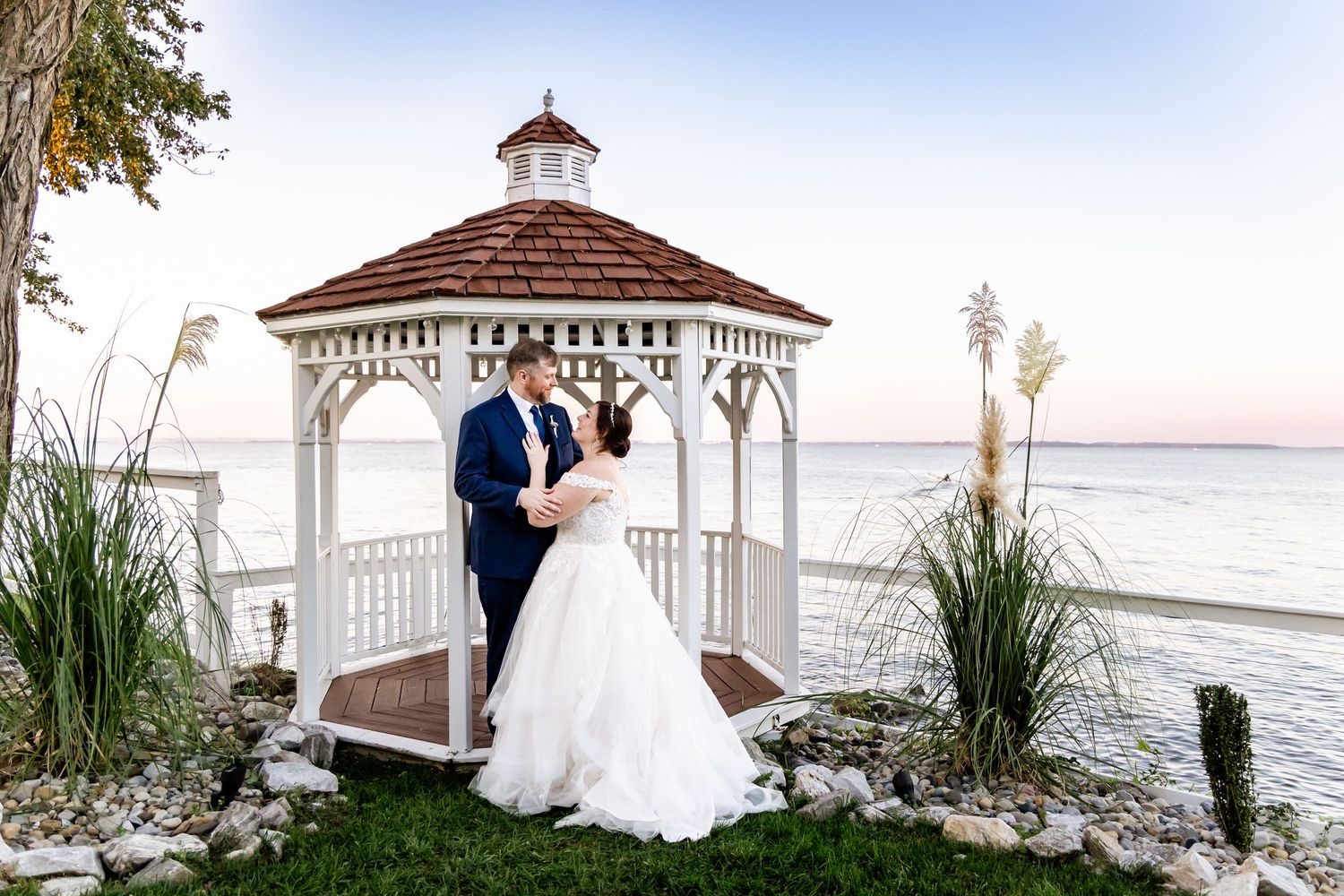 A romantic wedding ceremony takes place in a gazebo overlooking the ocean at sunset.