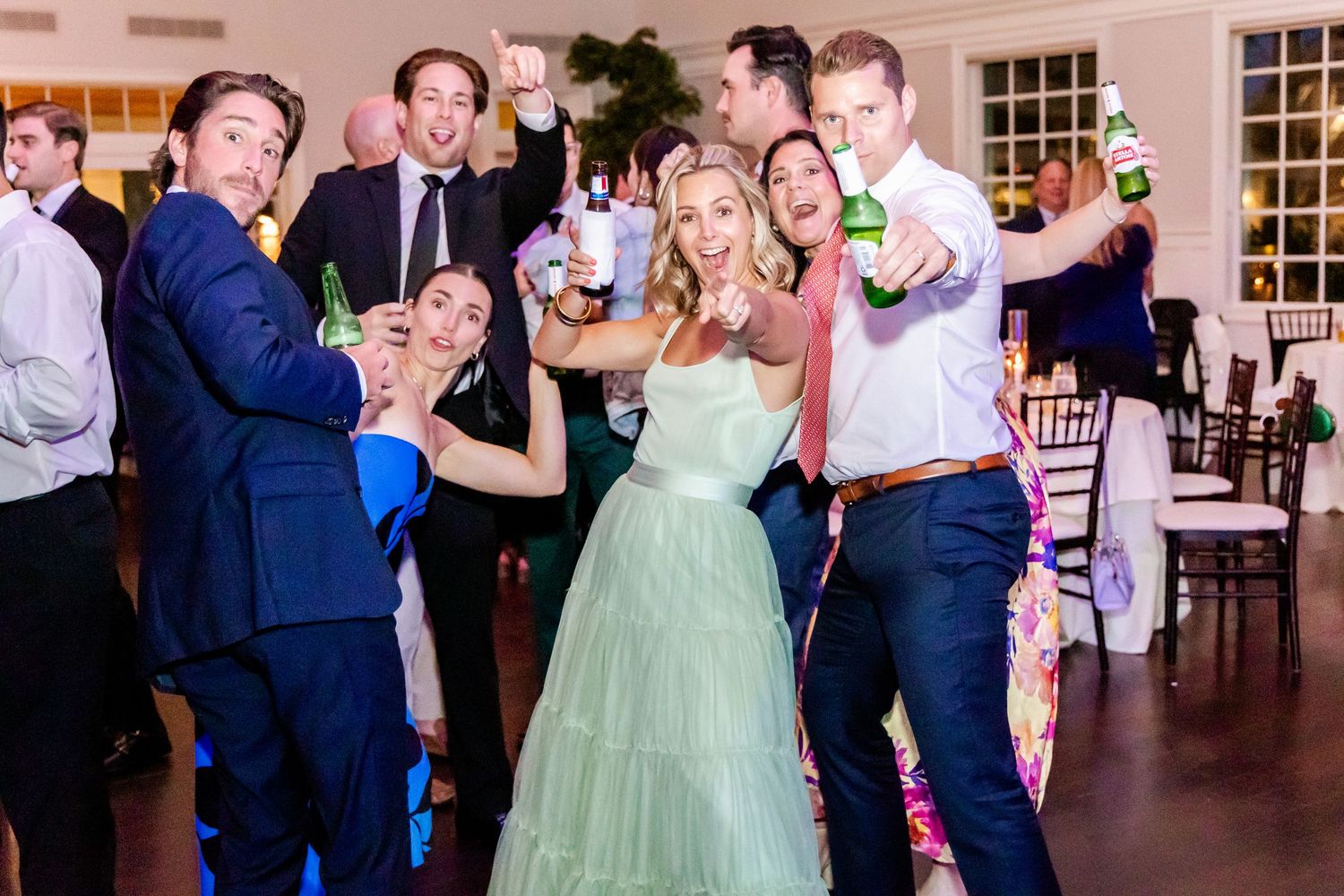 Wedding guests dancing and celebrating on the dance floor with a woman in a mint green tulle gown.