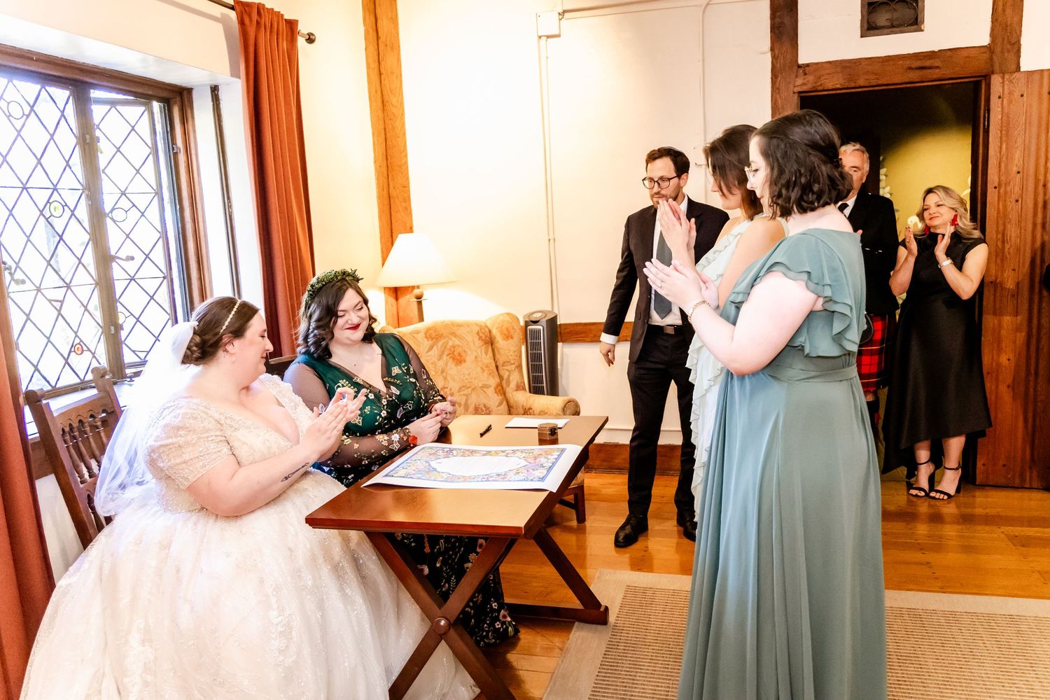 Wedding ceremony document signing moment with attendees gathered in an indoor setting with vintage decor.