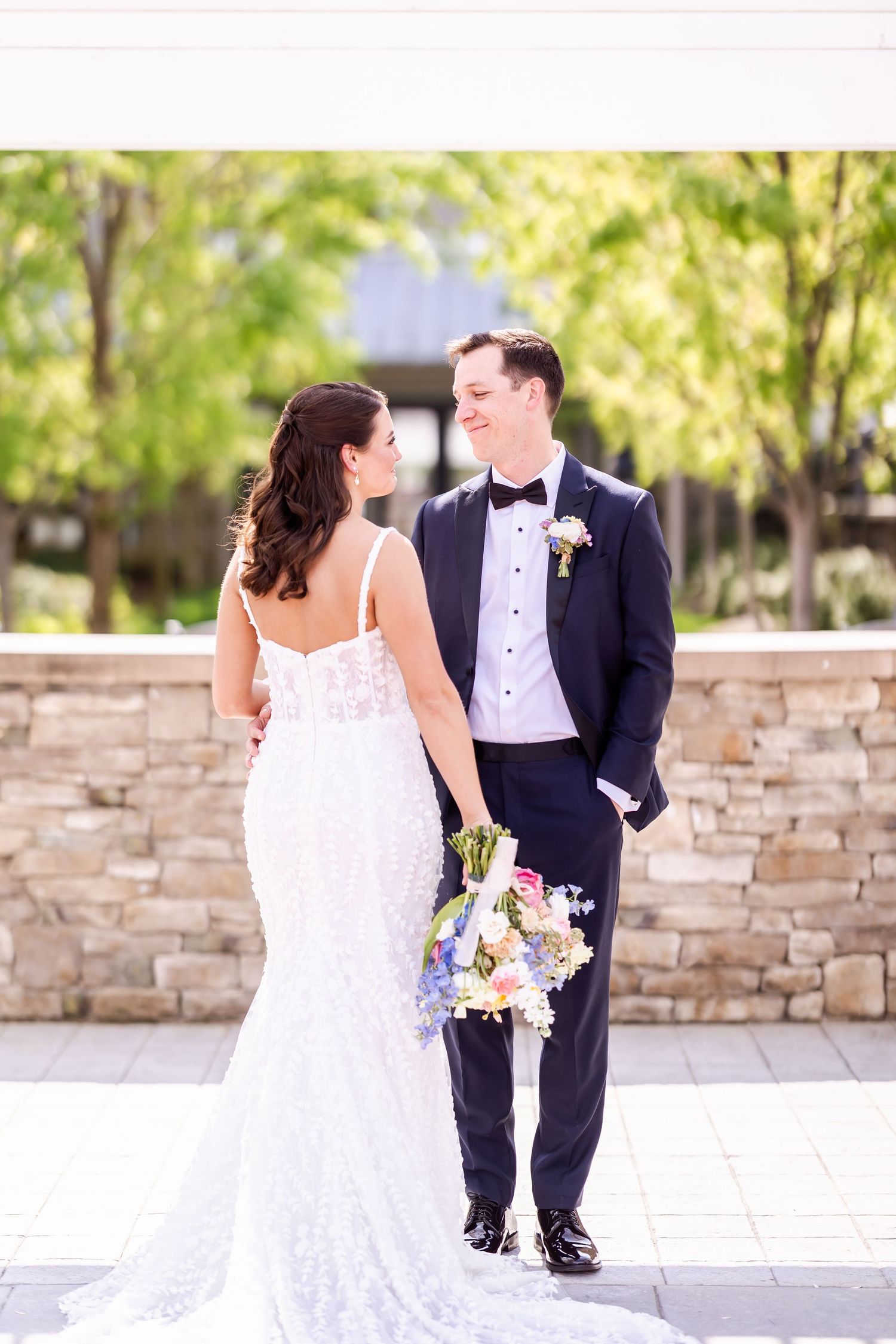 Newlyweds posing for romantic photos against a stone wall backdrop in natural sunlight.