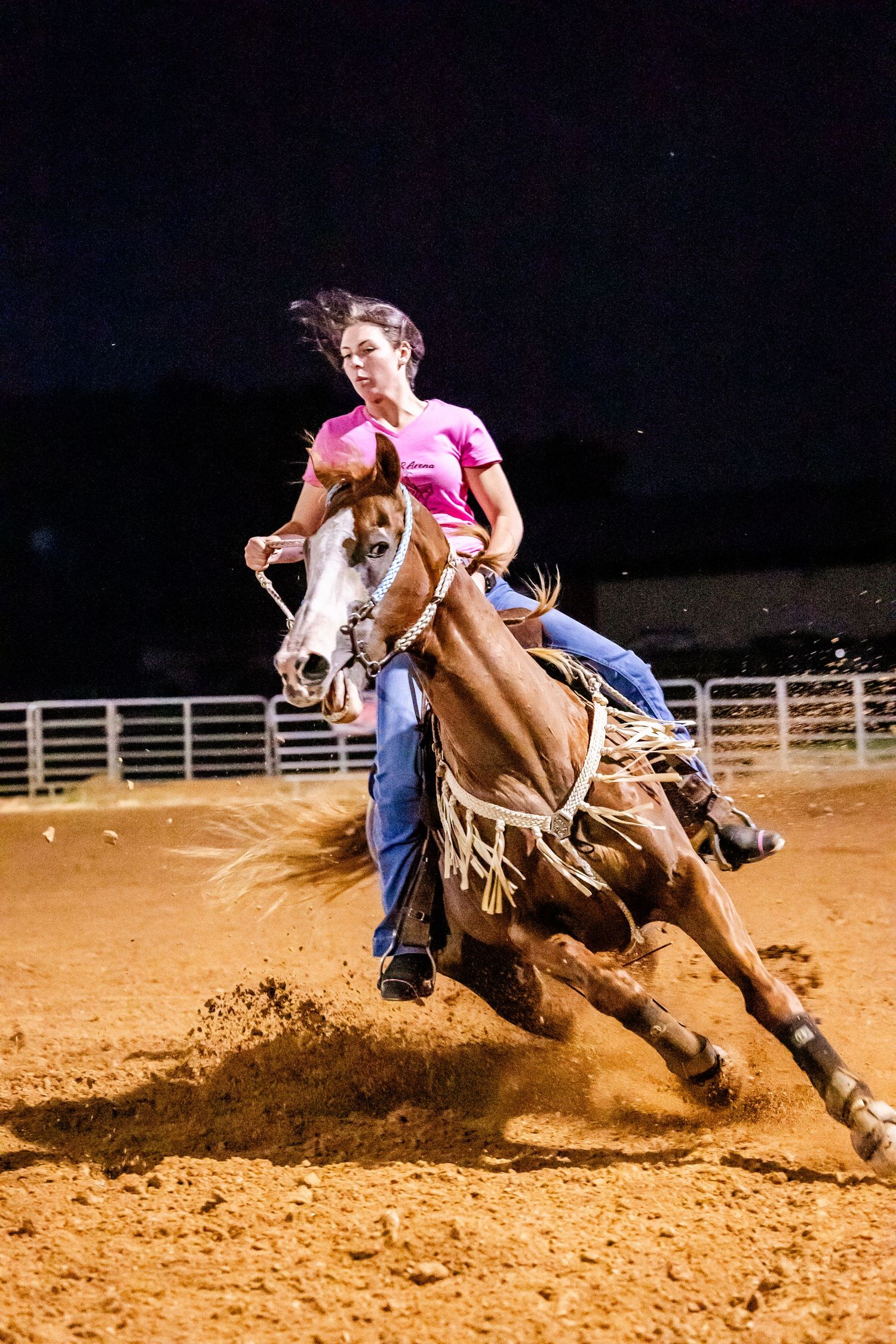 Horse and rider executing a sharp turn in barrel racing competition, kicking up dirt in the arena.