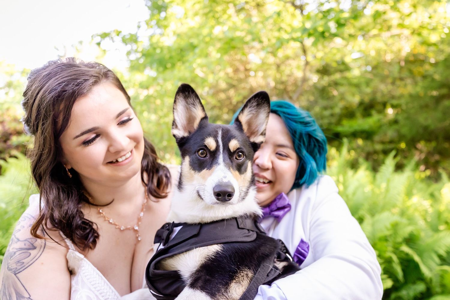 Couple shares joyful moment with their black and white dog against leafy garden backdrop.