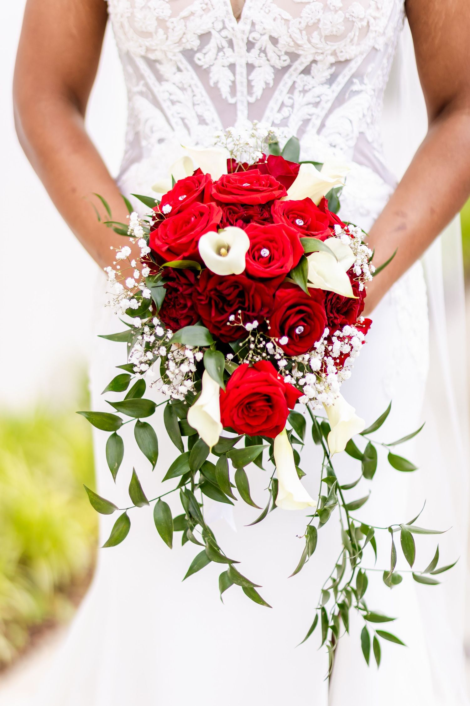 Close-up of a cascading bridal bouquet with red roses, white flowers and trailing greenery.