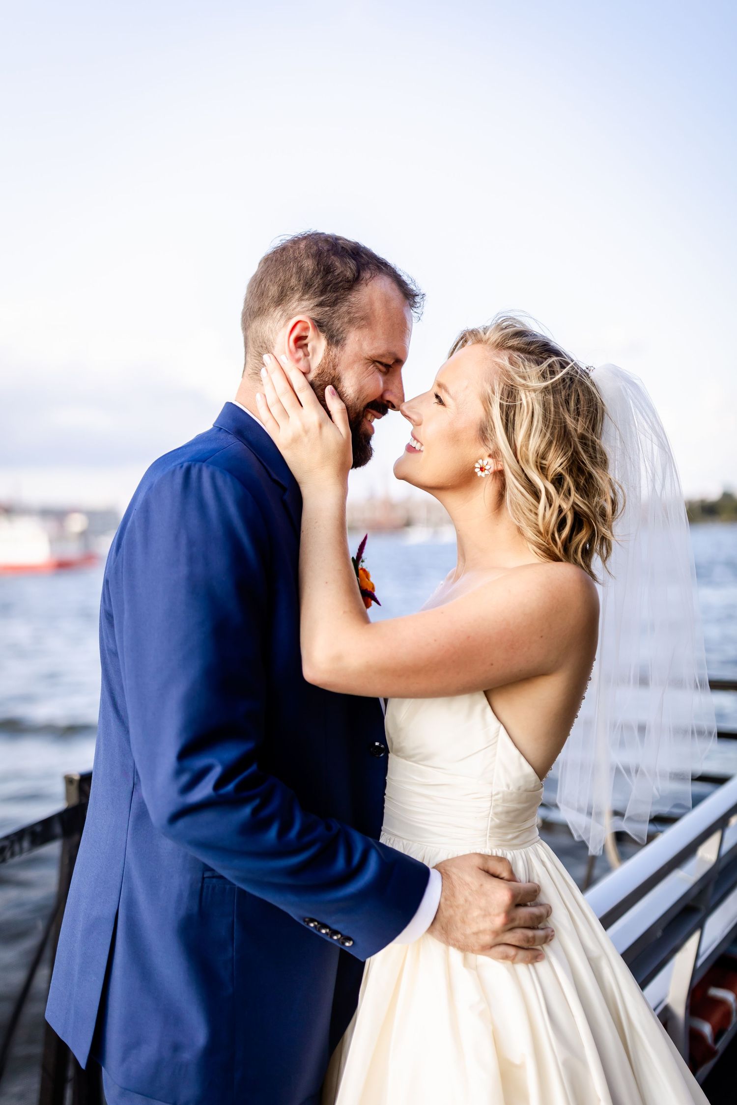 A romantic moment between newlyweds by the waterfront with boats in the background.