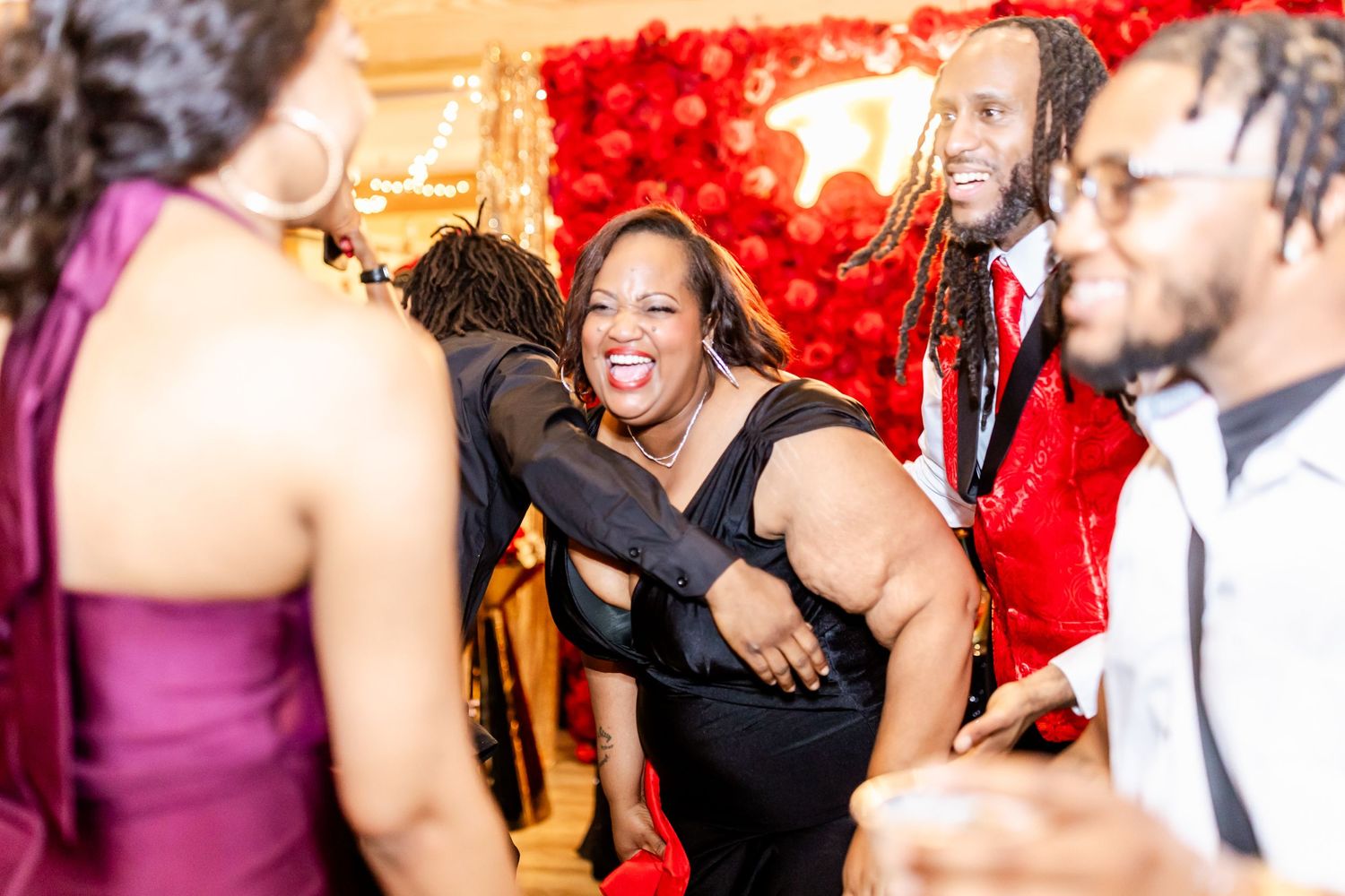 Energetic dancers enjoying themselves at a celebration with red decorations in the background.