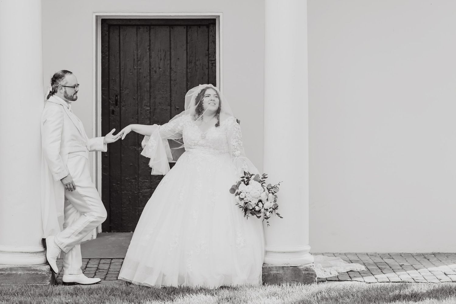 Black and white candid wedding moment captured in front of dark wooden door.