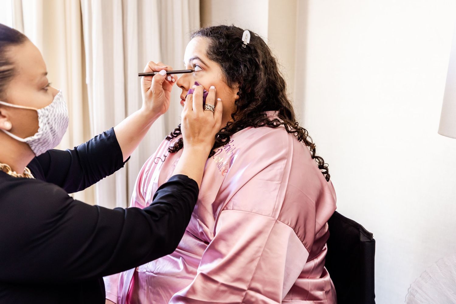 Wedding preparation scene with makeup application in a bright room.