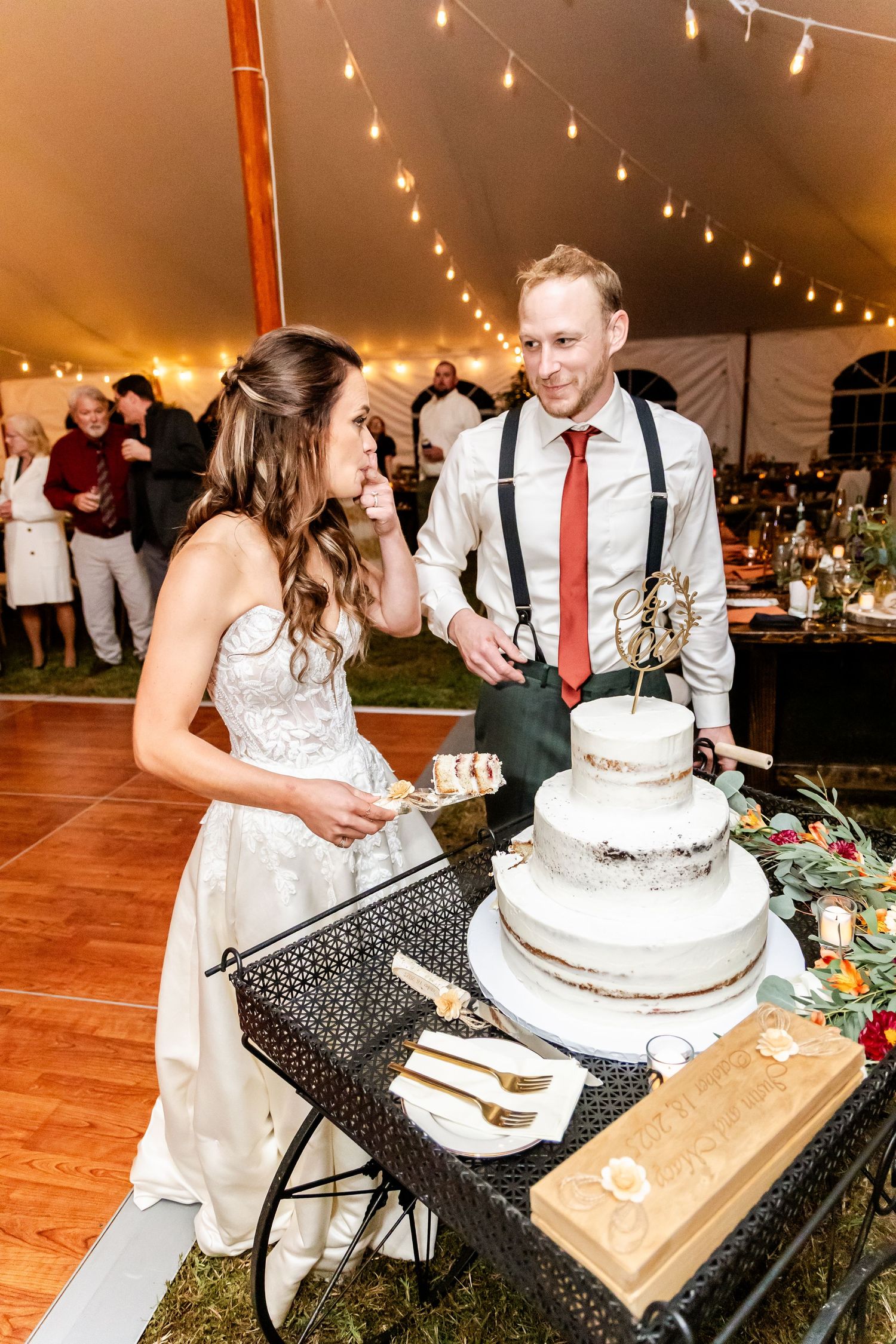 Traditional wedding cake cutting moment at reception under string lights.