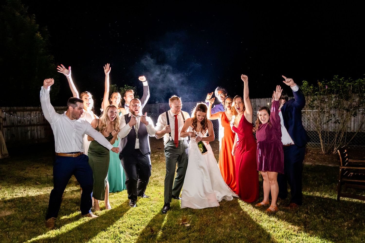 Wedding party celebrates with sparklers at night creating magical light trails.