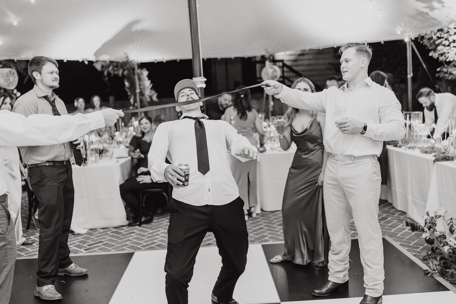 Black and white photo of wedding guests dancing and having fun on the dance floor under a tent.