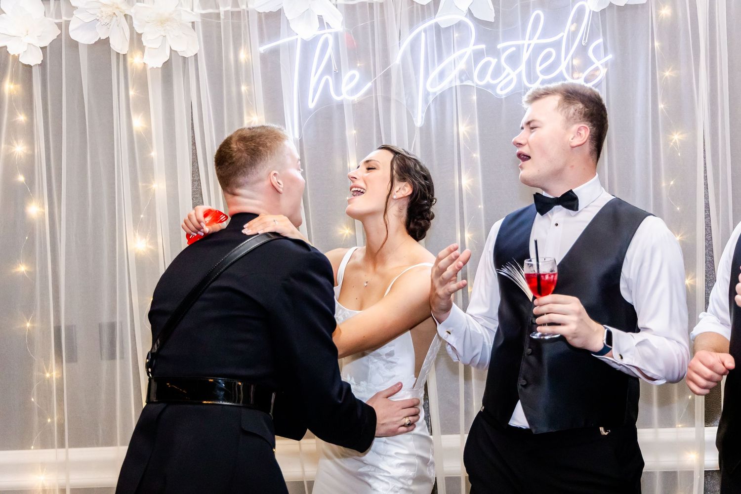Wedding party dancing under twinkling lights and decorative text signage at reception.